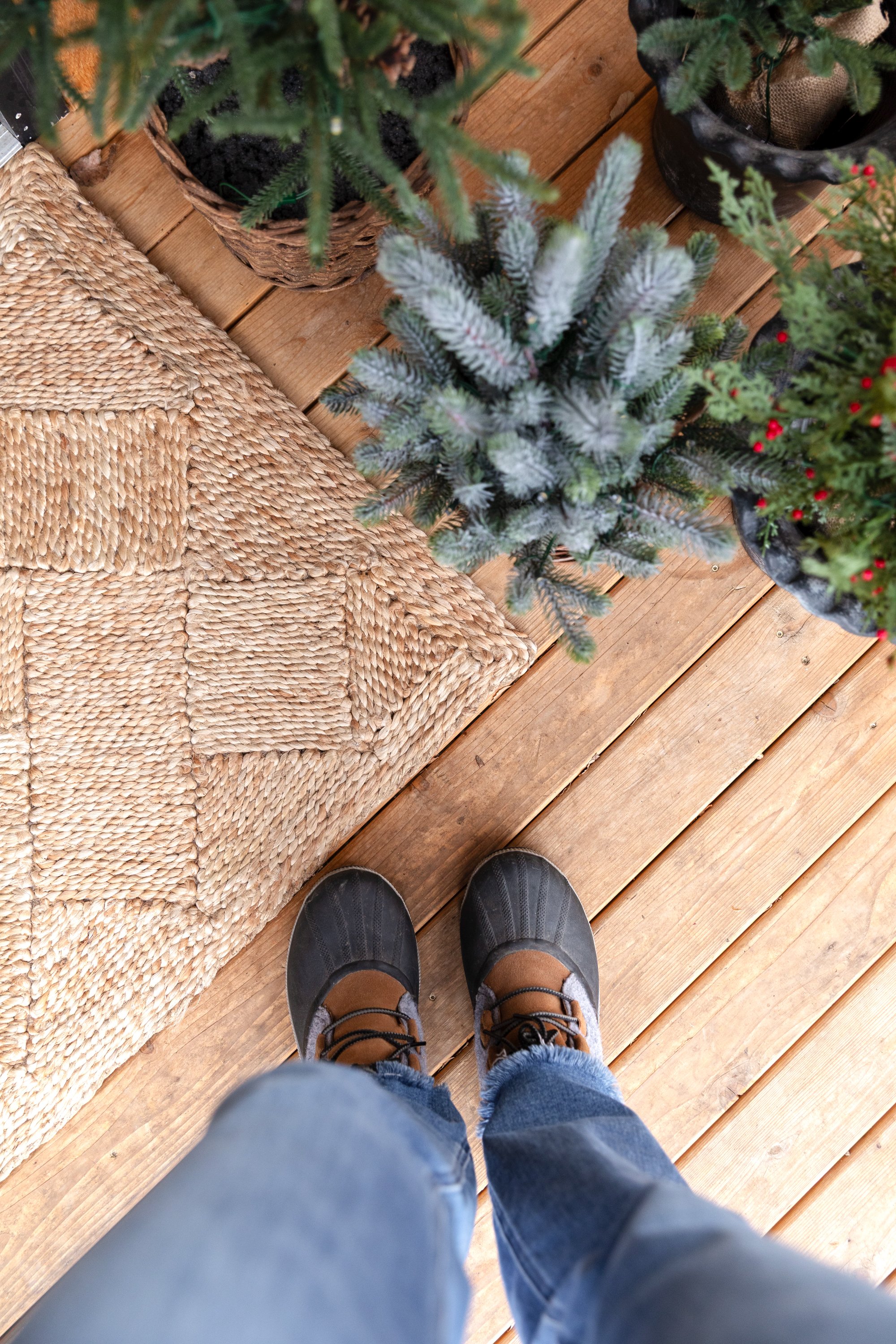 Holiday details on the Poplar Cottage front deck with jute rug, faux trees, and leather boots