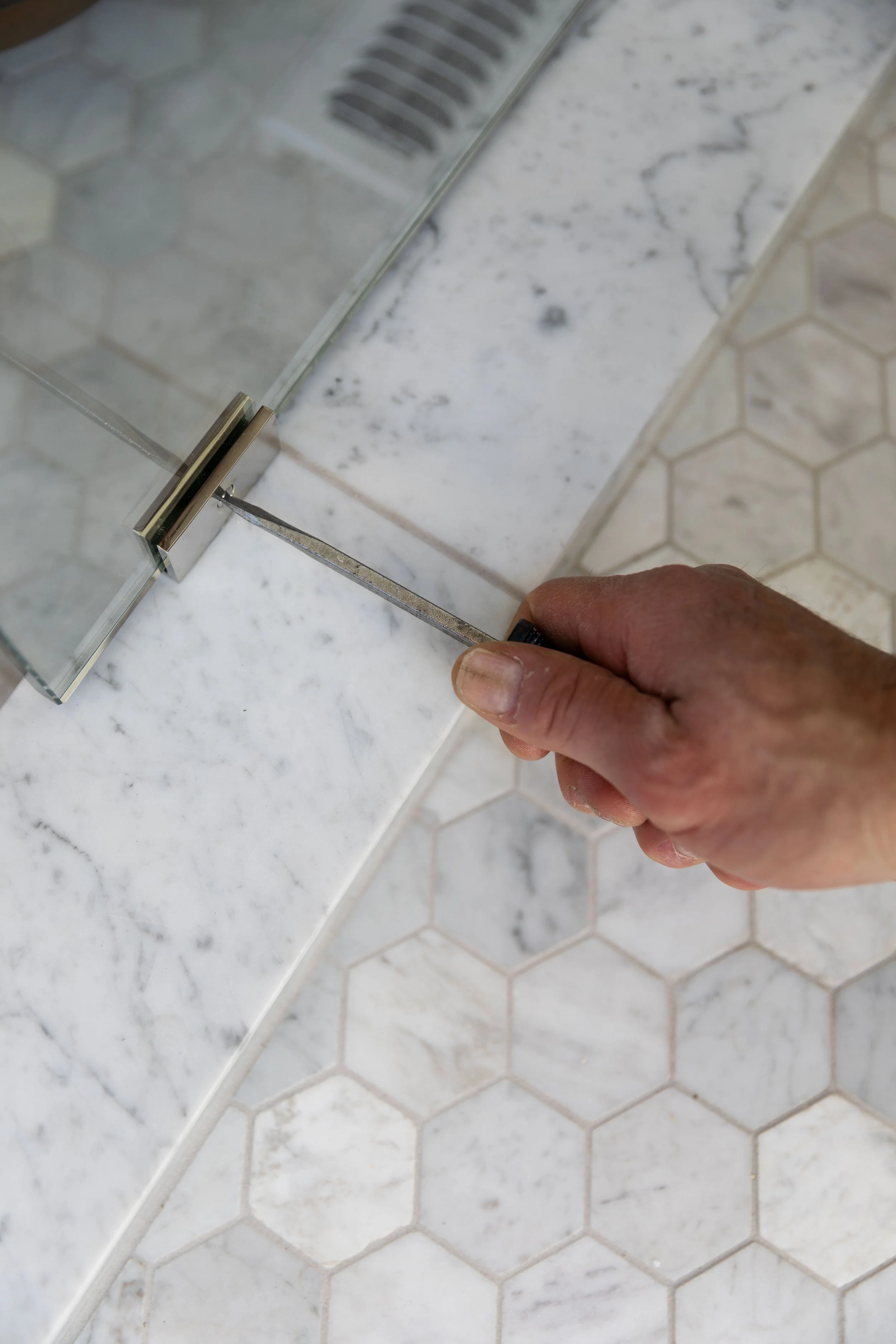 Close-up of a glass shower panel clip being installed on a marble curb