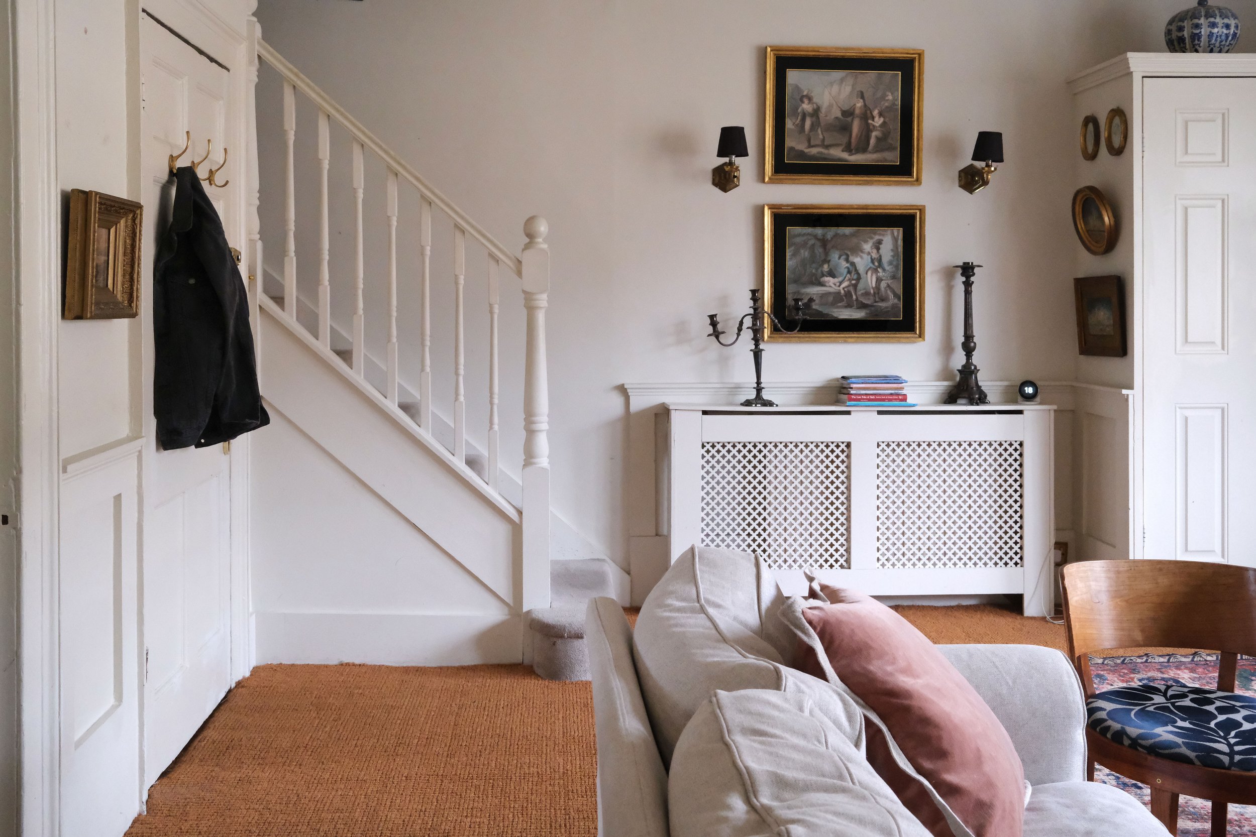 White living room in a historic Bath apartment with vintage art, antique furniture, and layered rugs
