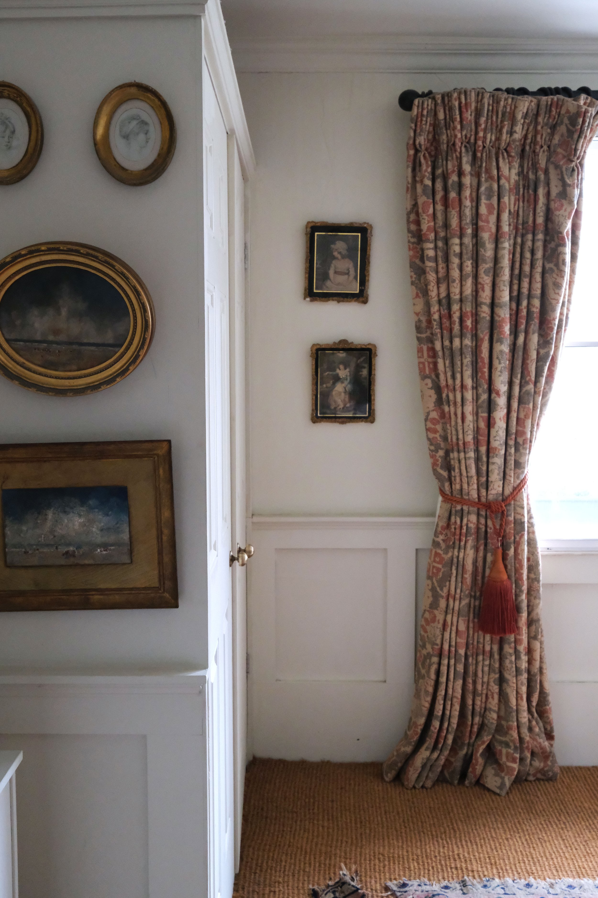 Collection of vintage paintings and gilt frames on the white walls of an English living room