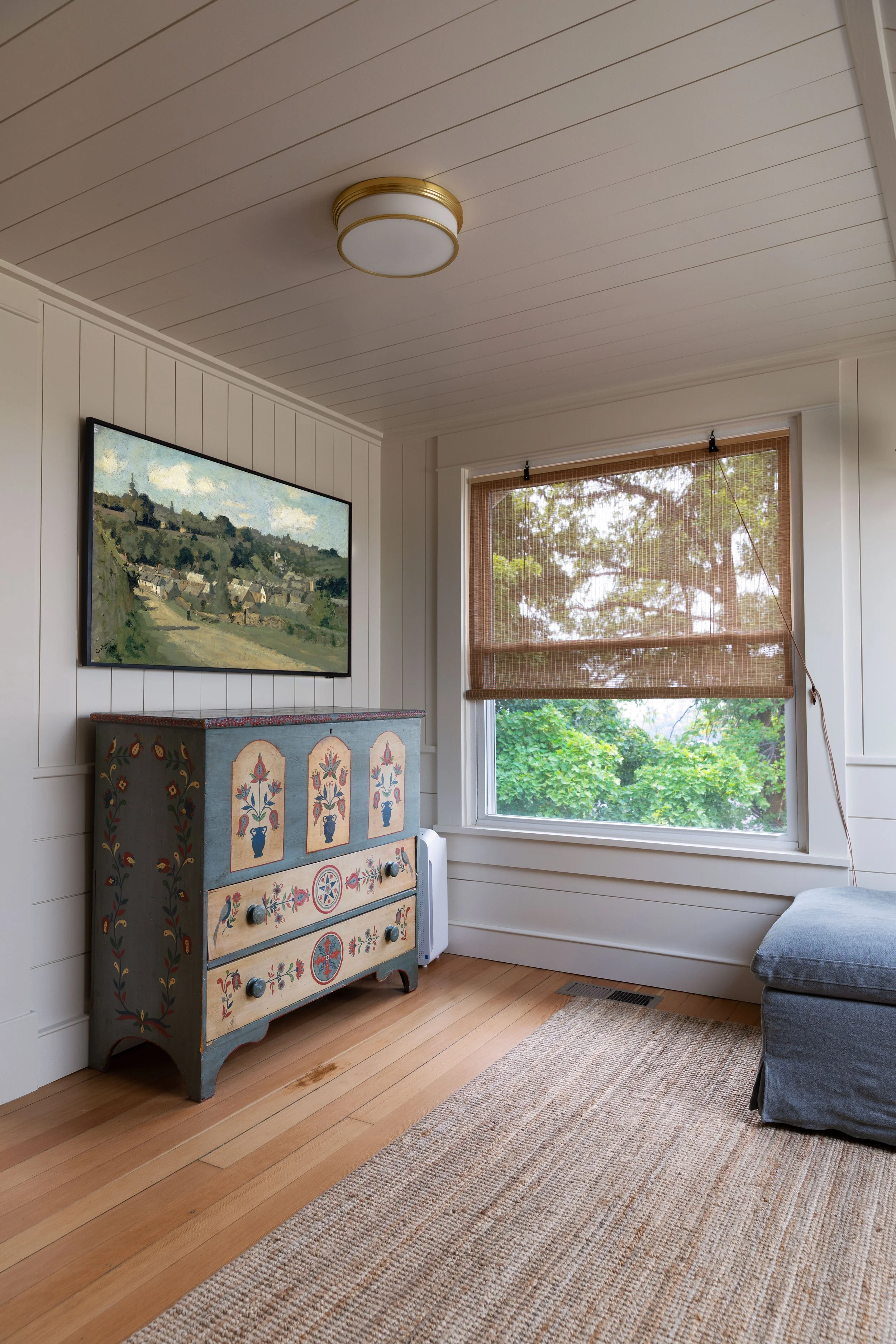 White paneled walls, bamboo window shade, handprinted dresser, and frame tv in the upstairs snug