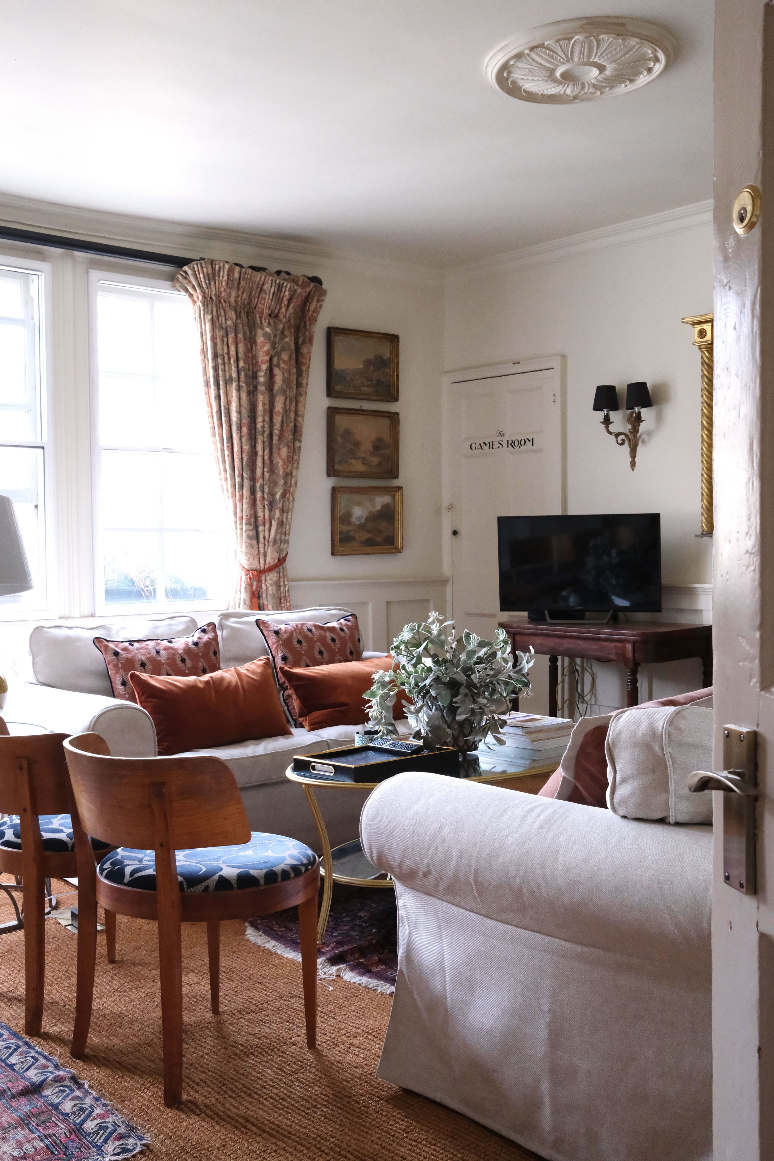 White living room in a historic Bath apartment with vintage art, antique furniture, and layered rugs