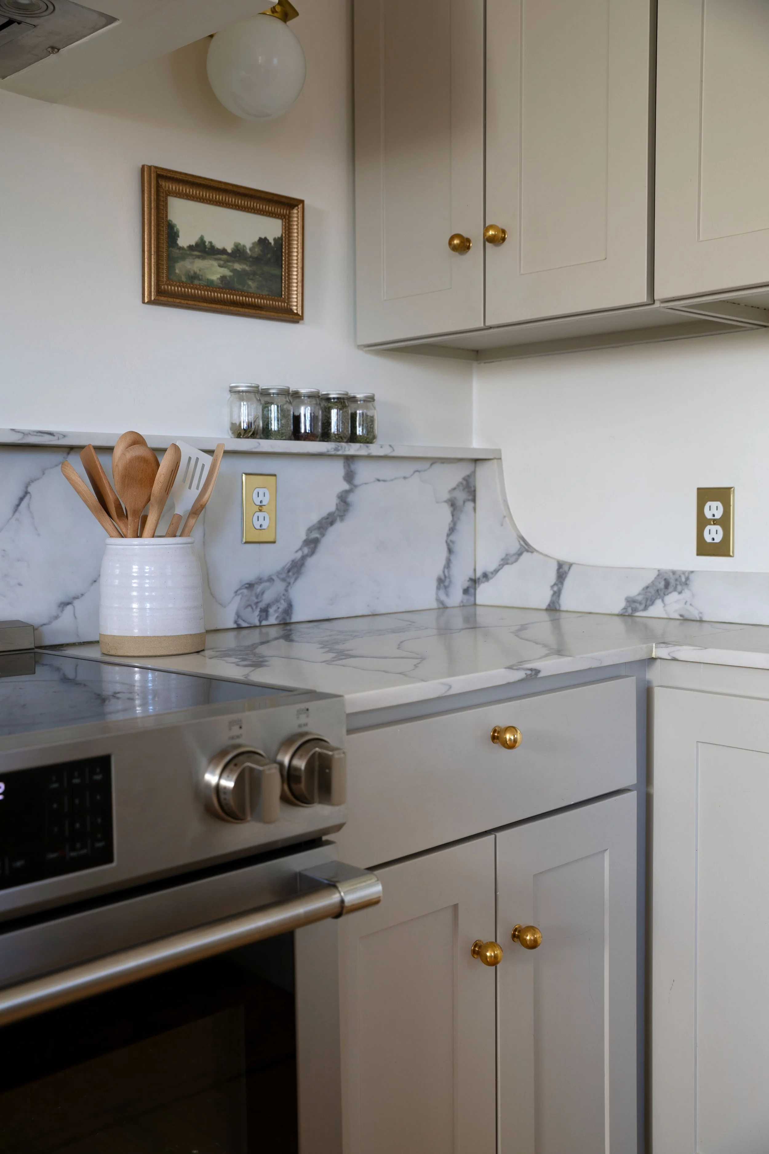 Close-up of quartz backsplash with 12-inch curve, brass hardware, and painted cabinetry.