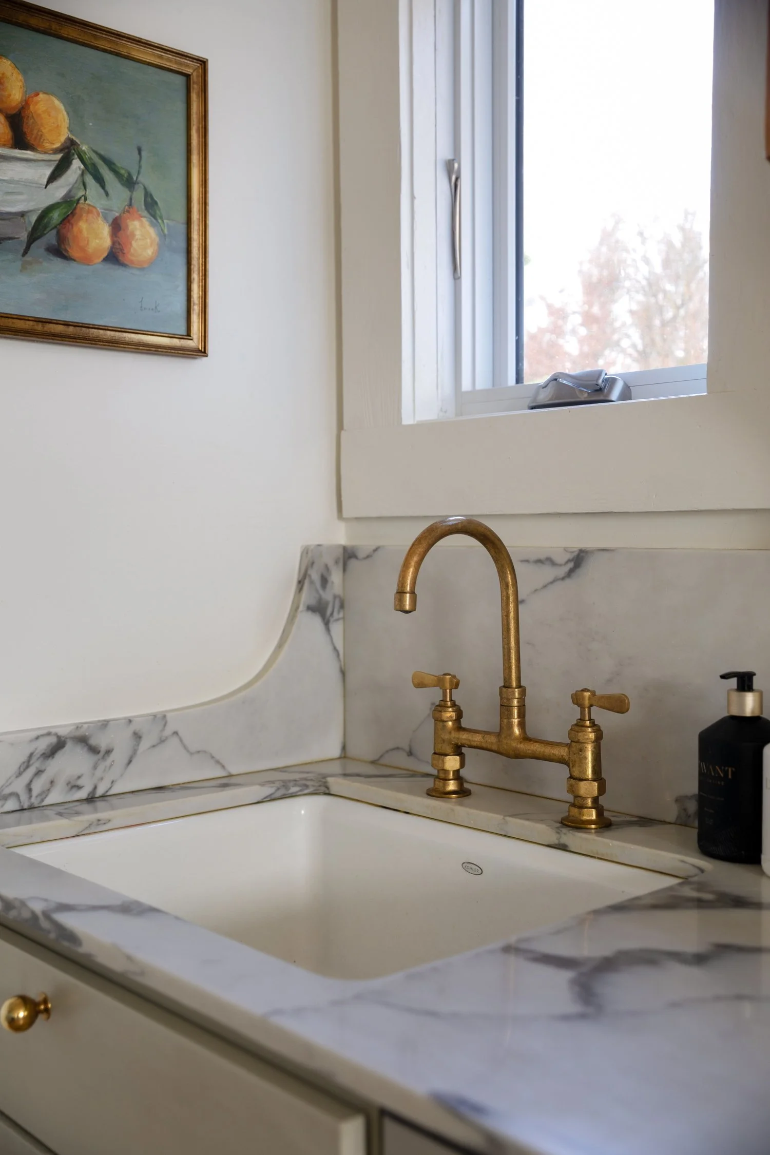Close-up of Kohler cast iron sink, unlacquered brass faucet, and quartz backsplash curve.