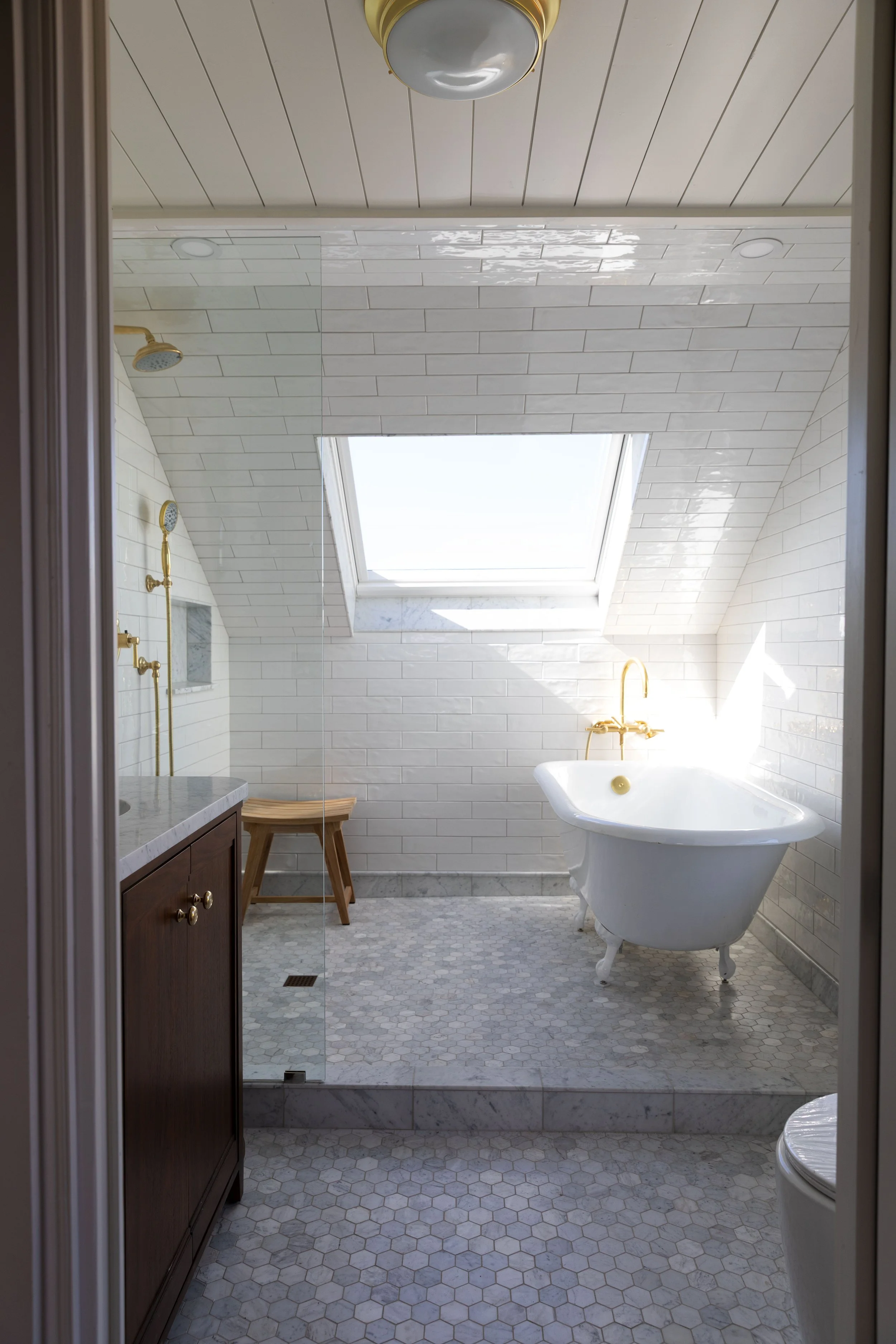 White bathroom wet room with a clawfoot tub, frameless glass shower, and skylight