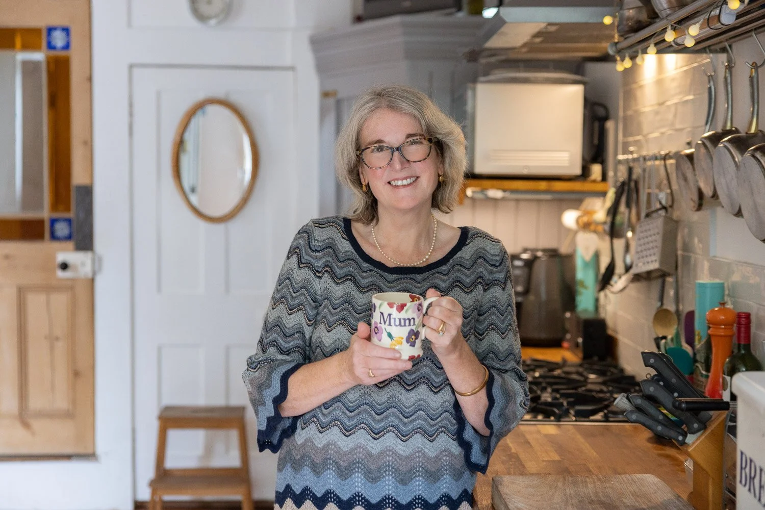 Personal branding photography in London showing a confident but natural expression of a female business owner standing in a kitchen holding a cup of coffee