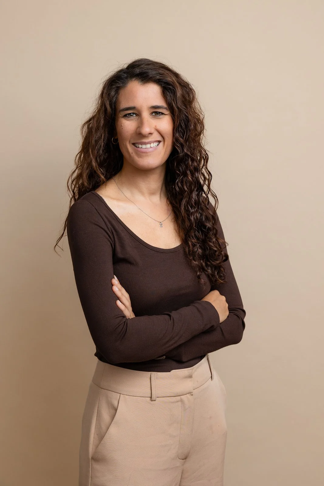 Corportae headshot of a lady against a beige backdrop, looking to camera smiling naturally