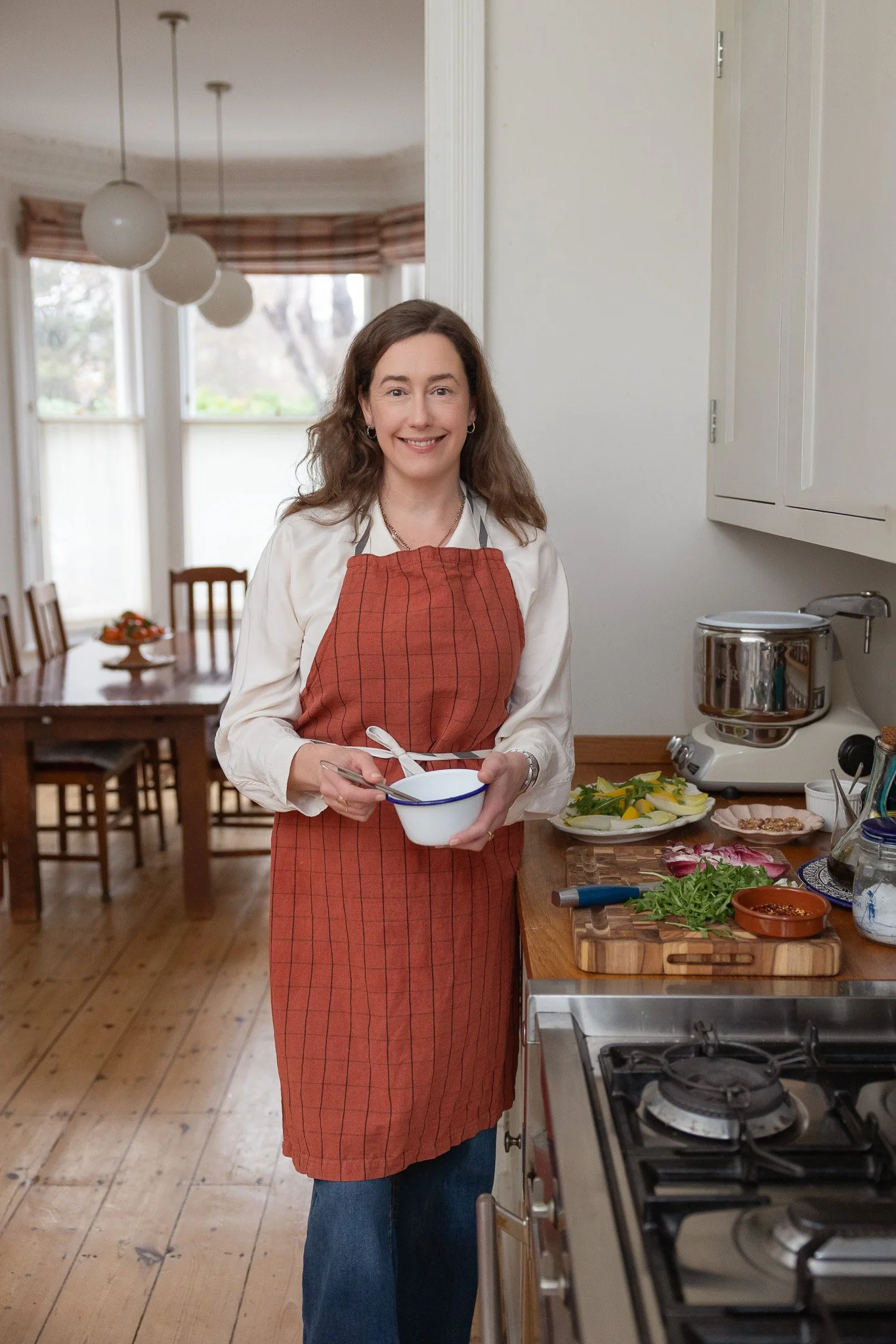 Personal Branding photography showing a female nutritionist standing in a kitchen preparing food. She is wearing an apron and is smiling.