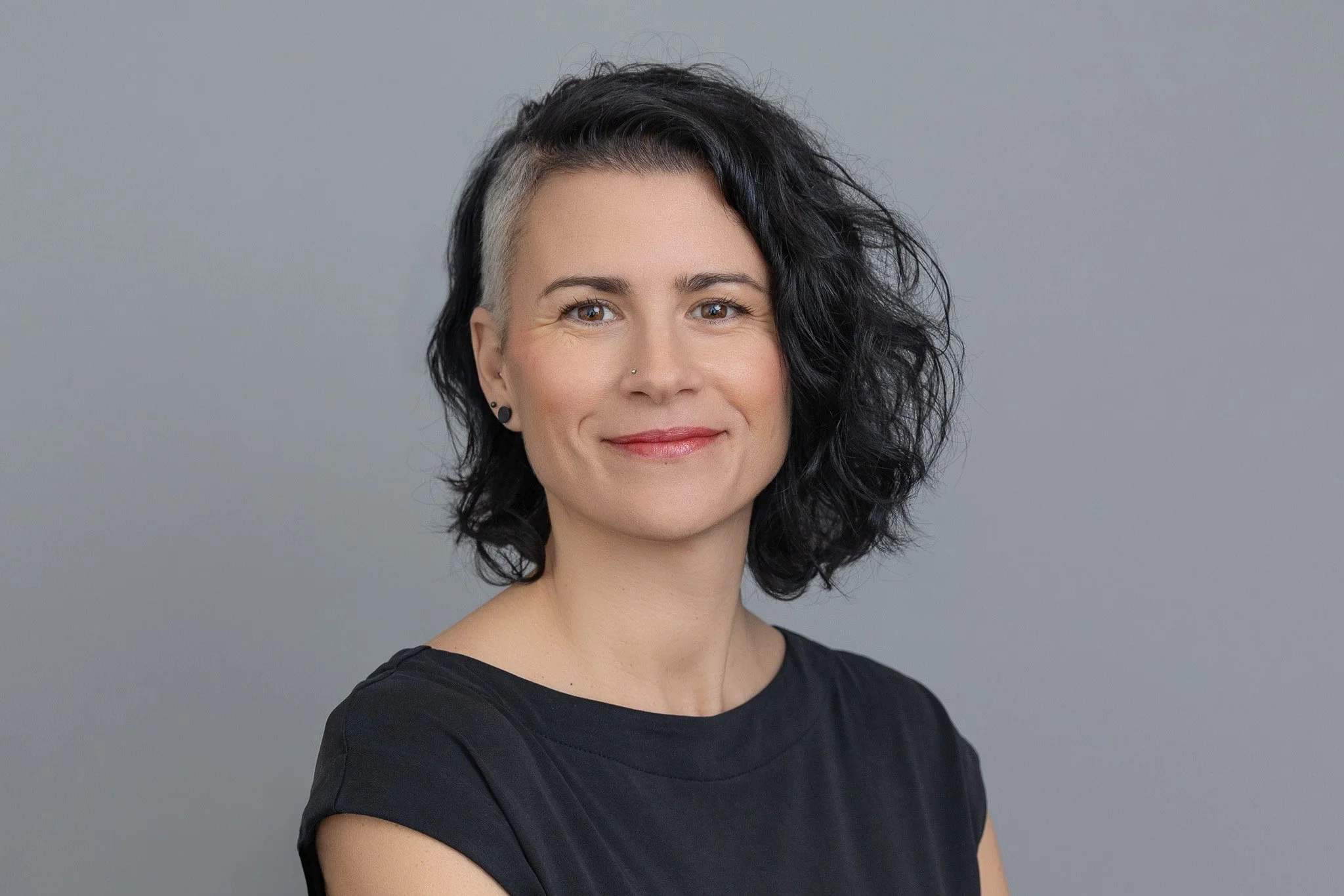 Corporate headshot of a lady looking to camera with a natural smile, against a grey backdrop