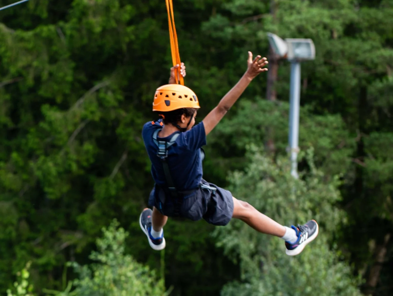 Ung pojke som åker zipline i skogsmiljö, bär hjälm och sele.