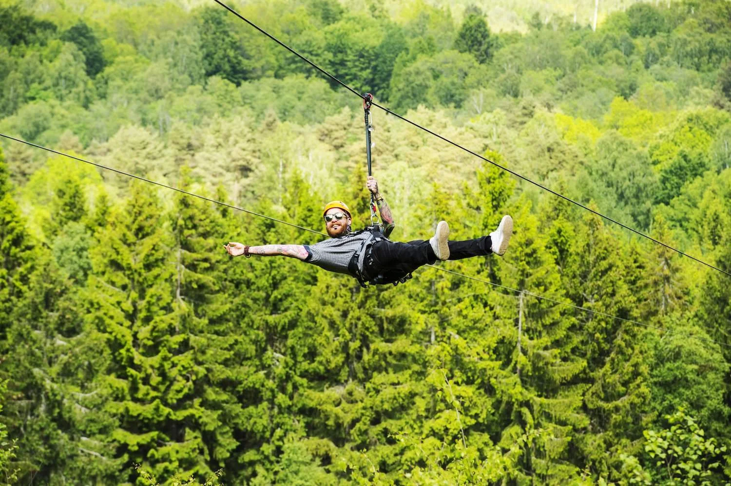 En man i säkerhetsutrustning åker zipline över en grön skog.