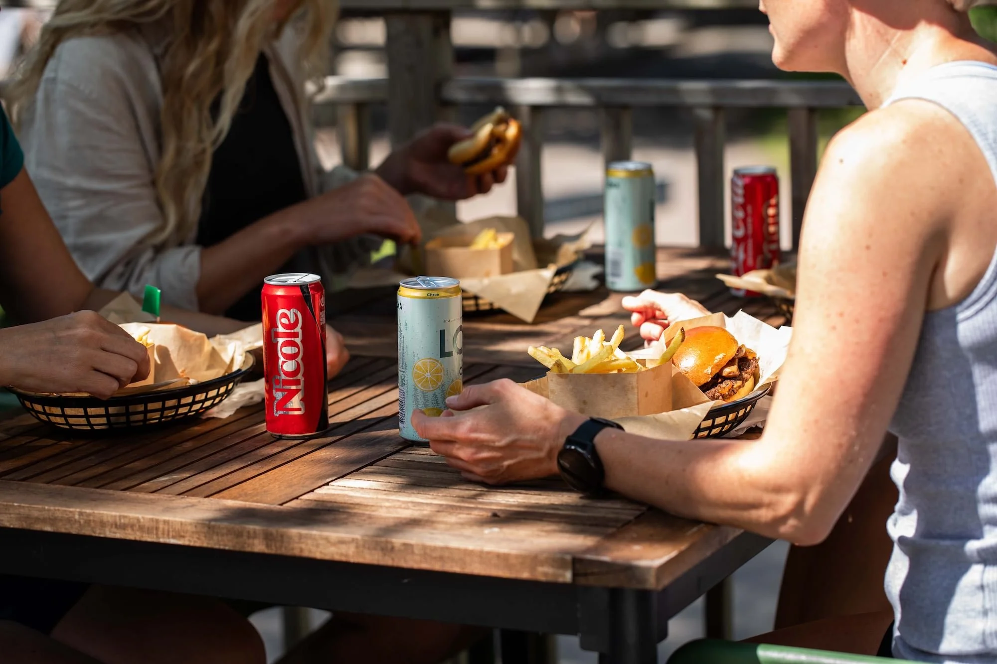 Människor som äter hamburgare och dricker läsk på en restaurang utomhus.