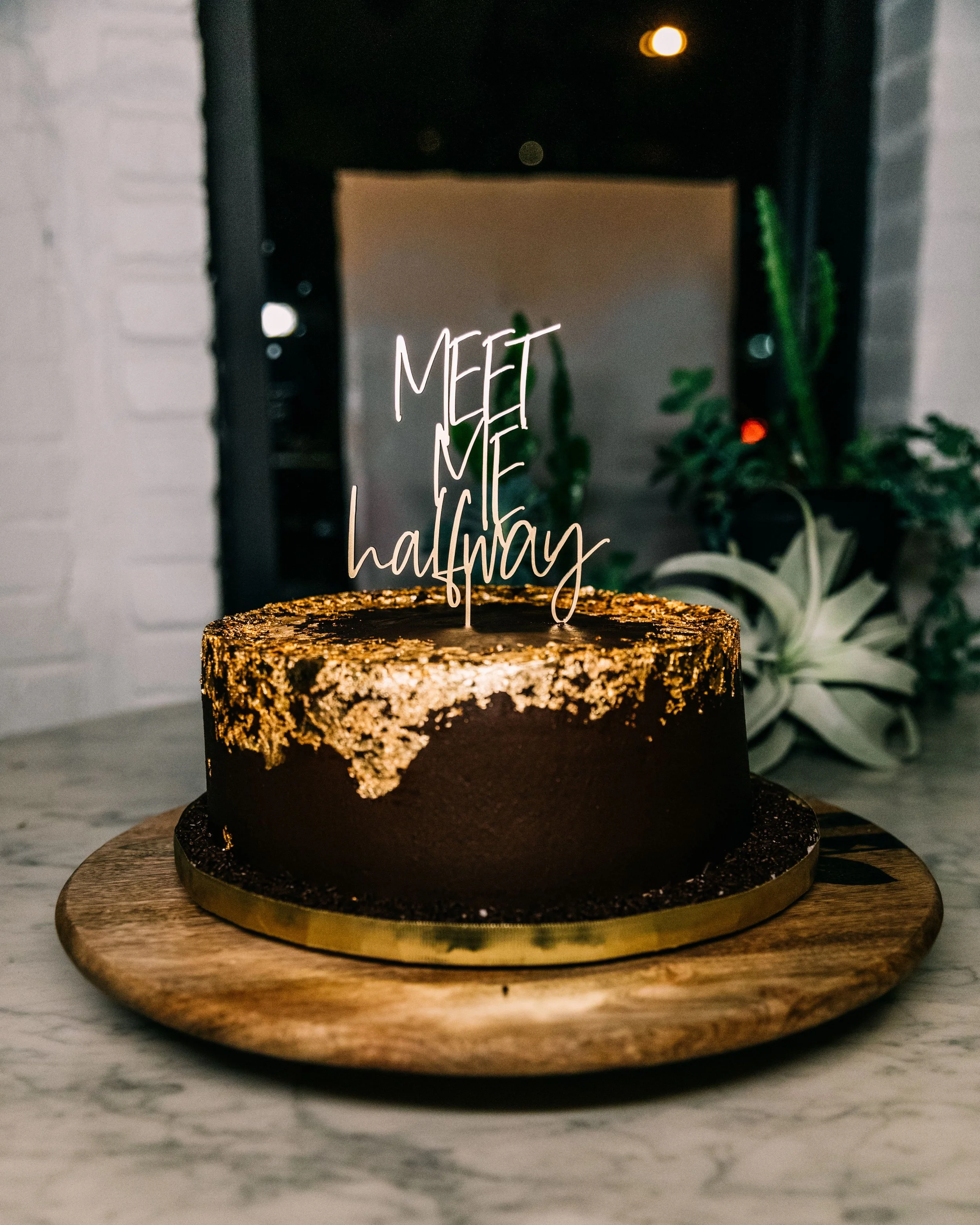 Layered Dark Chocolate cake with gold foil on top and a sign stating "Meet Me Halfway" on the top.