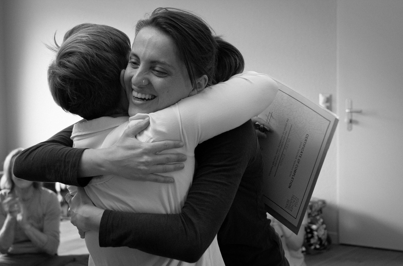 Two women hugging in celebration, one holding a diploma, in black and white.