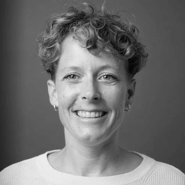 Black and white portrait of a woman with short curly hair, smiling, wearing hoop earrings and a light-colored sweater.