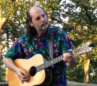 As a toddler, Ellis Ralph spent every waking and sleeping hour hearing the music from his older sister’s AM radio. Those were the days. Around age five, he was indelibly influenced by Anita B., the landlady and family friend downstairs who masterfully belted out songs over the sound of her lawnmower or her old Chevy pickup, making singing seem like . . . something normal people might do. By age eight, Ellis had sung to open several annual recitals where his older sister danced, making singing seem like . . . something predestined. As a tweenager, he learned personally from the fabulous Louis Blue, a free spirited minstrel who was the spit and image of Woody Guthrie, that he could figure out just about ANYthing with only three amazing chords! Ellis maintained a life-long, part-time, secret-identity as a singer-songwriter, performing in closets or with various esoteric cults, using song to solve all of humanity’s intractable problems, such as romance, theology, and internal rhymes. Then, around the turn of the century, as the strain and stress of Y2K and the unrelenting responsibilities of adulthood started to become . . . old, Ellis felt called to come out, to acknowledge that he had always been a singer-songwriter trapped in the body of a workaholic, and to embrace: Fun.