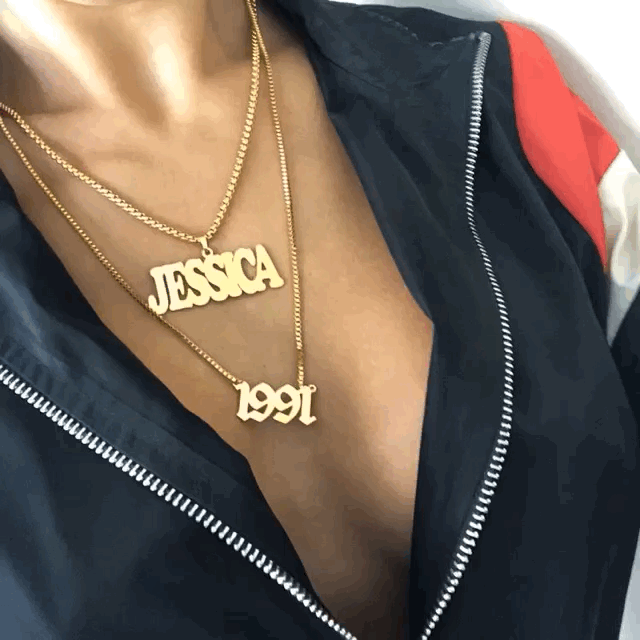 Close-up of a person wearing two gold necklaces, one with the name 'Jessica' and the other with the year '1991', on a dark zippered jacket.