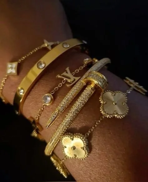 Arm adorned with multiple gold and diamond bracelets, featuring luxury designer logos and floral motifs.