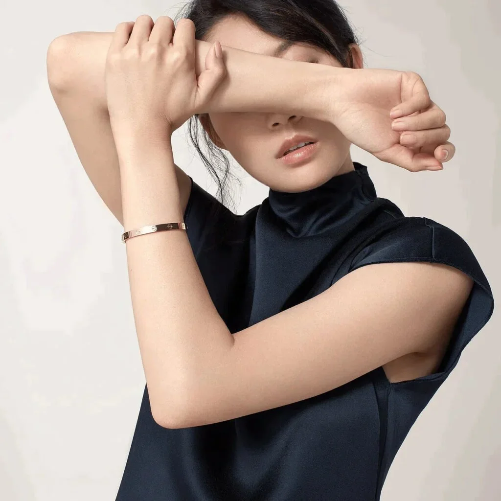 Woman in black dress covering face with arms, wearing a bracelet.