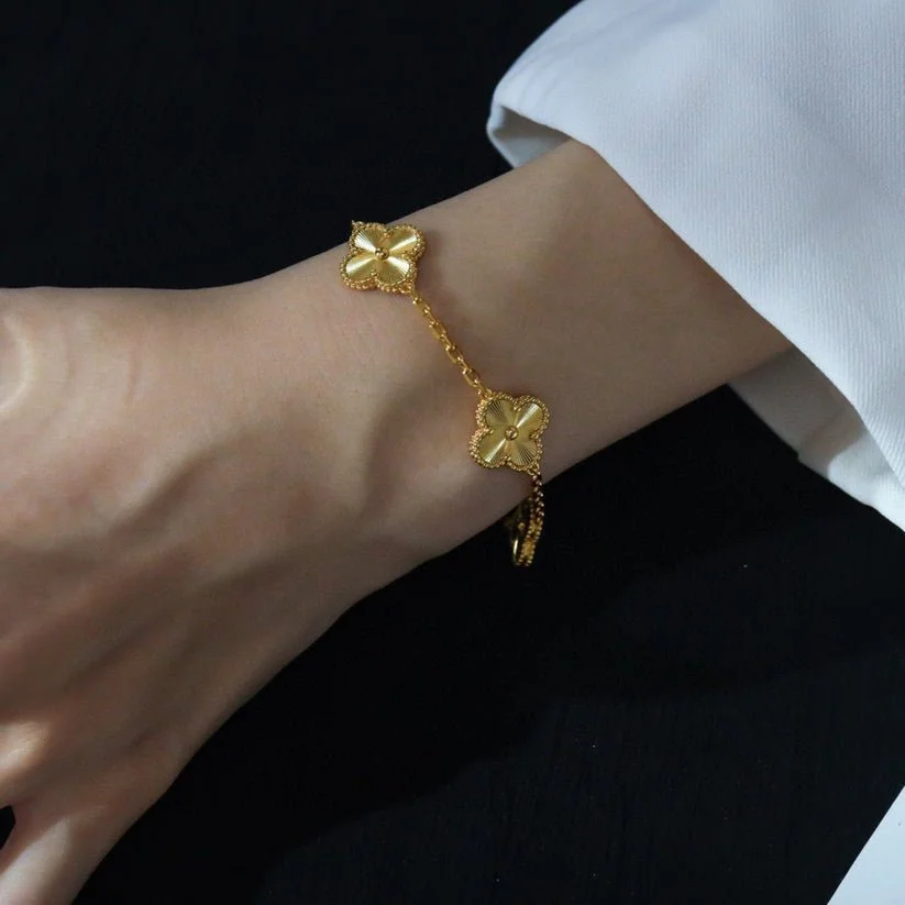 Gold clover charm bracelet on a person's wrist with a white sleeve background.