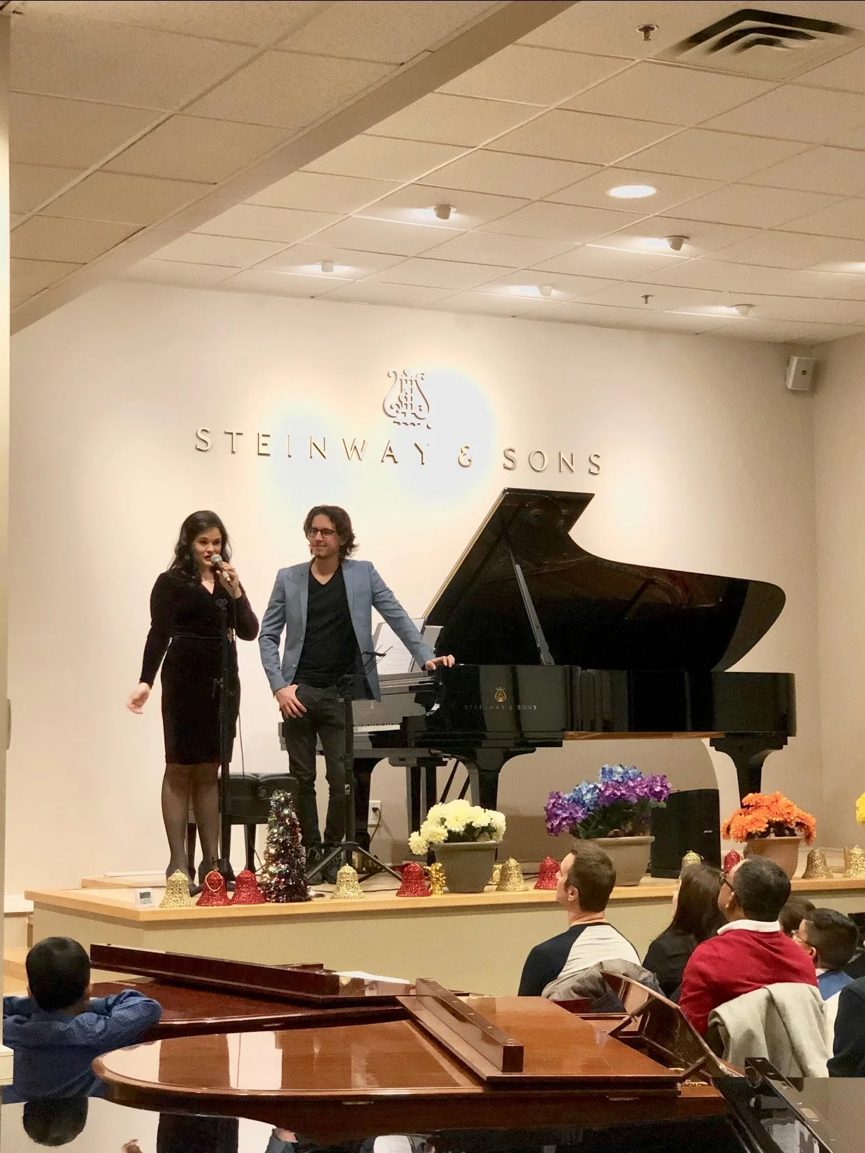 Andy Kitusa on the stage at the Steinway & Sons Gallery hosting an AK Music recital. Audience members are seated and watching performances take place on the world''s finest piano: a Steinway Model D.