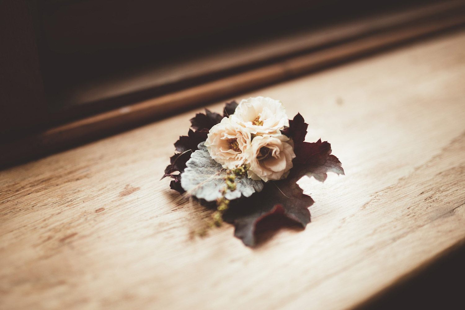 Buttonhole with red leaves and cream roses in window