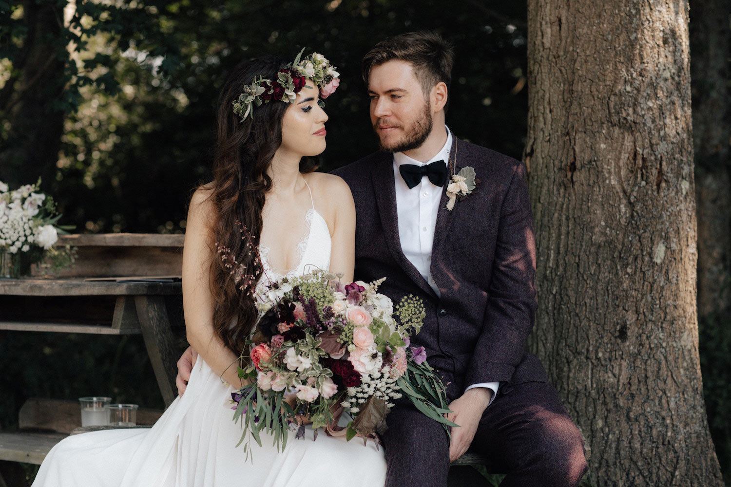 Bohemian bride and groom sitting in woodland ceremony