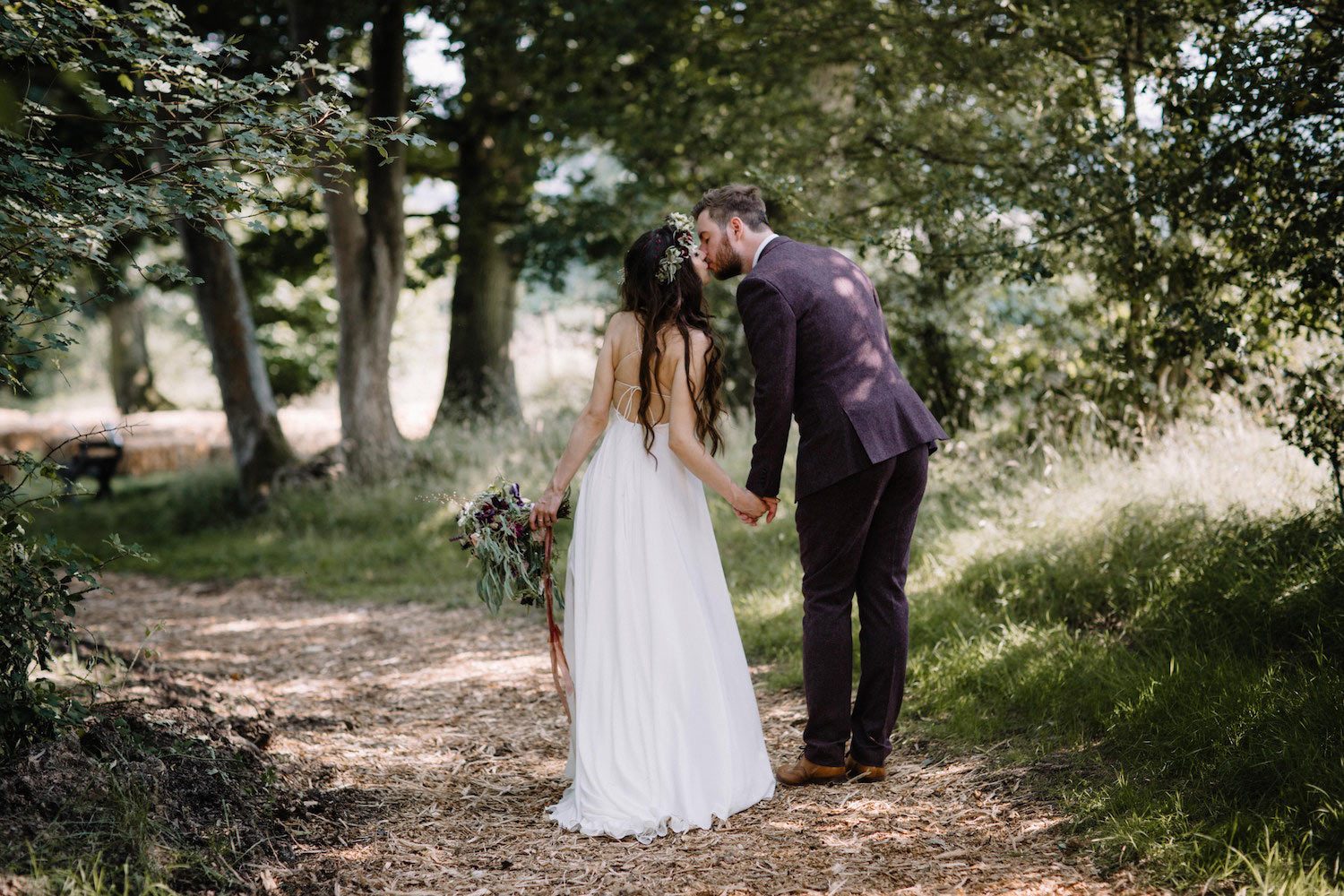 Bohemian bride and groom kissing in woodland path 