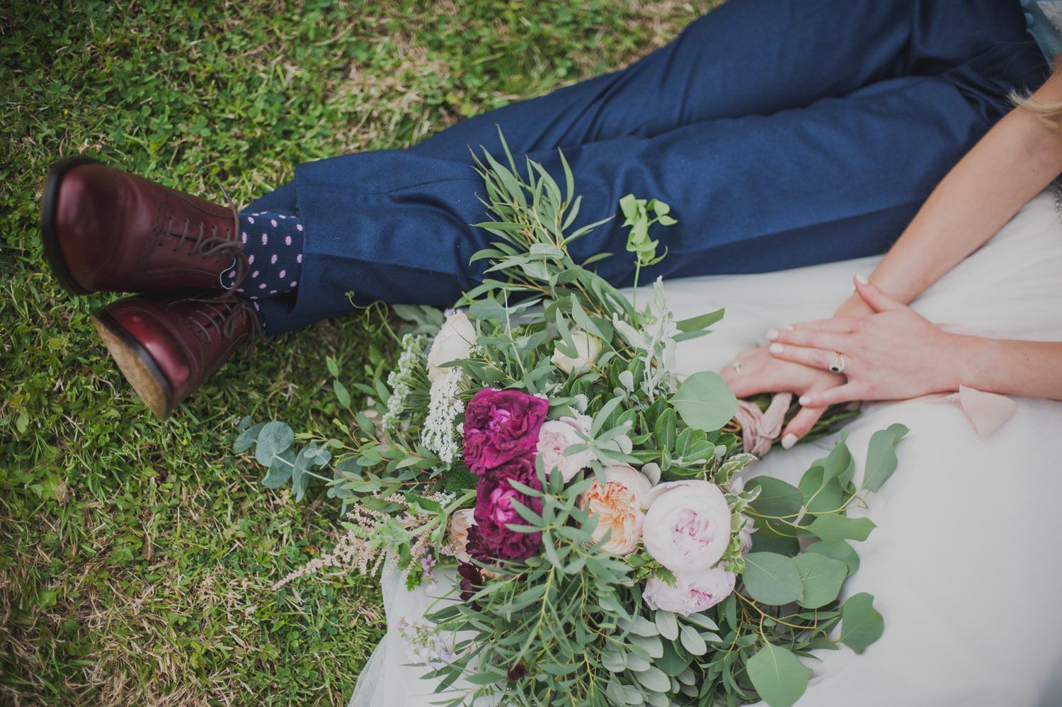 Bride and groom sitting in grass with flowers