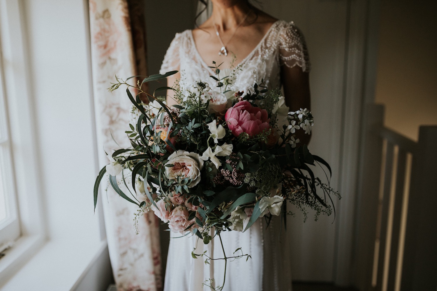 Bride standing by window holding bouquet