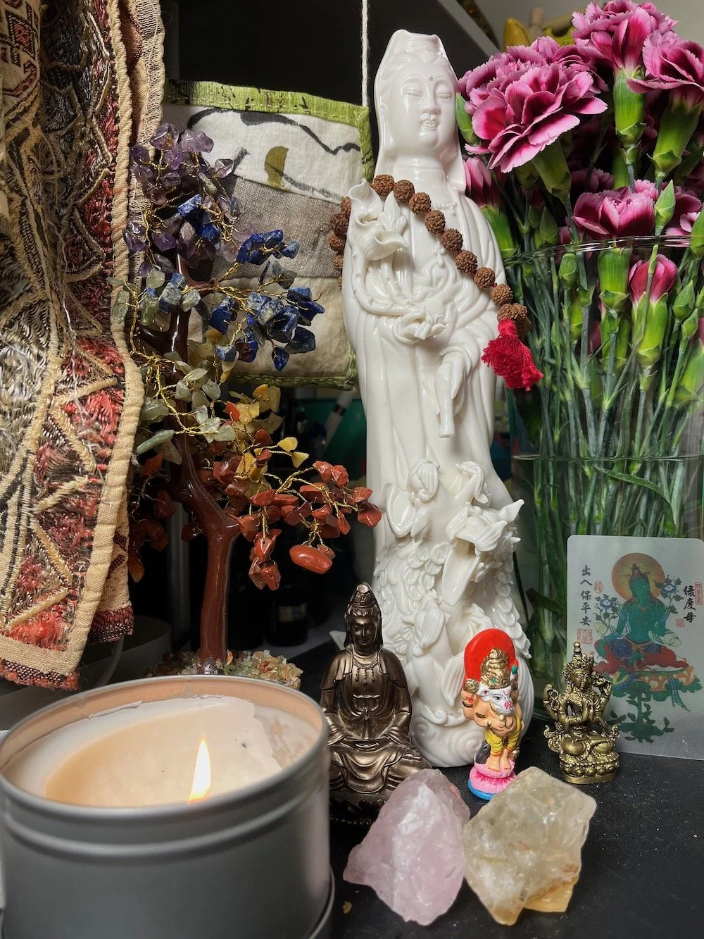 Decorative altar with various statues, flowers, a candle, and crystals.
