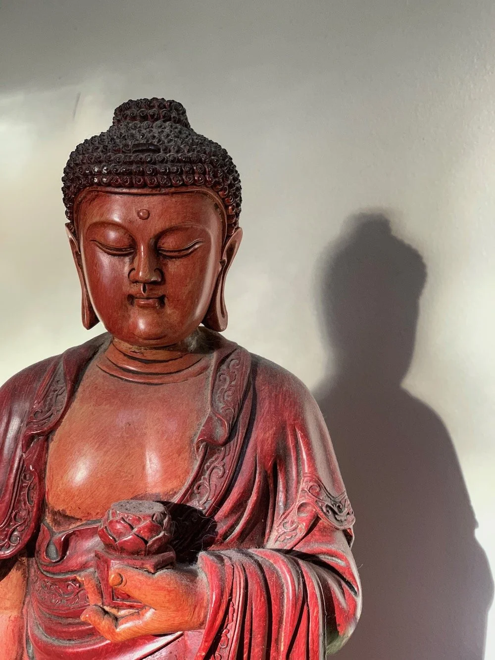 Wooden statue of Buddha with closed eyes, detailed hair, and a serene expression, casting a shadow on the wall behind.