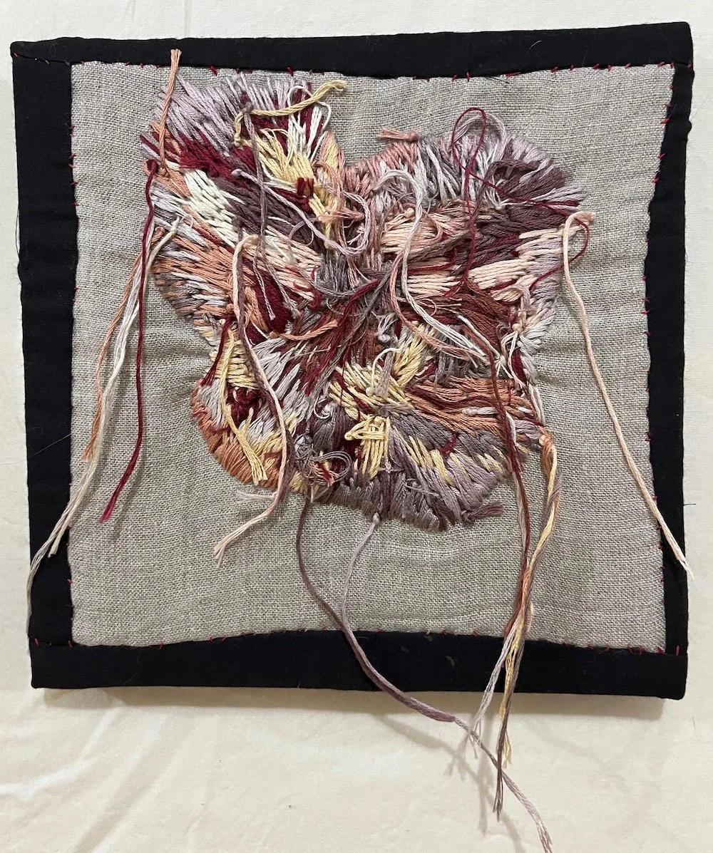 Abstract textile art piece with tangled multicolored thread on a beige square fabric background, framed with black border stitched with red thread.