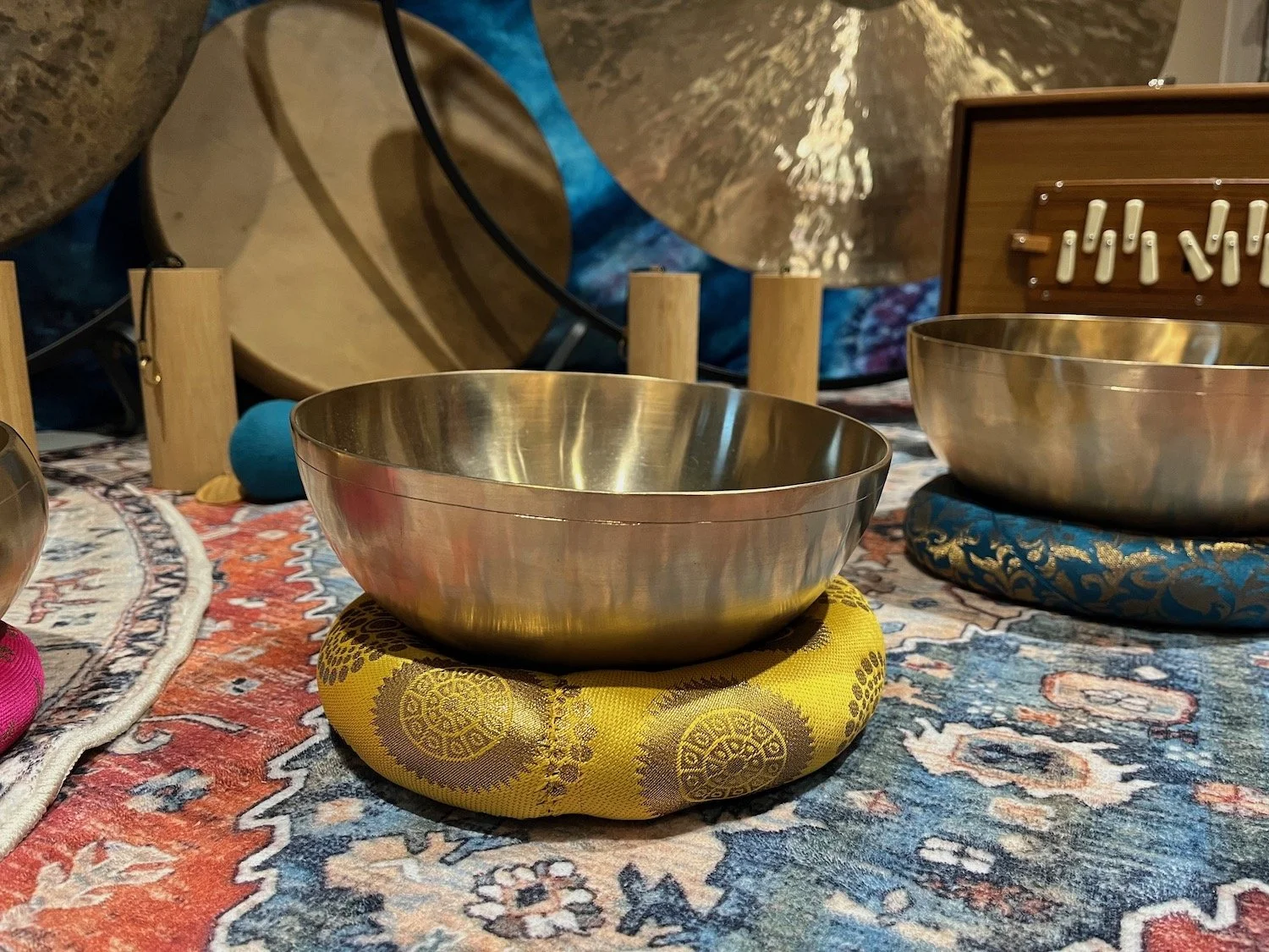 Close-up of metallic singing bowls placed on colorful fabric cushions on a patterned rug.