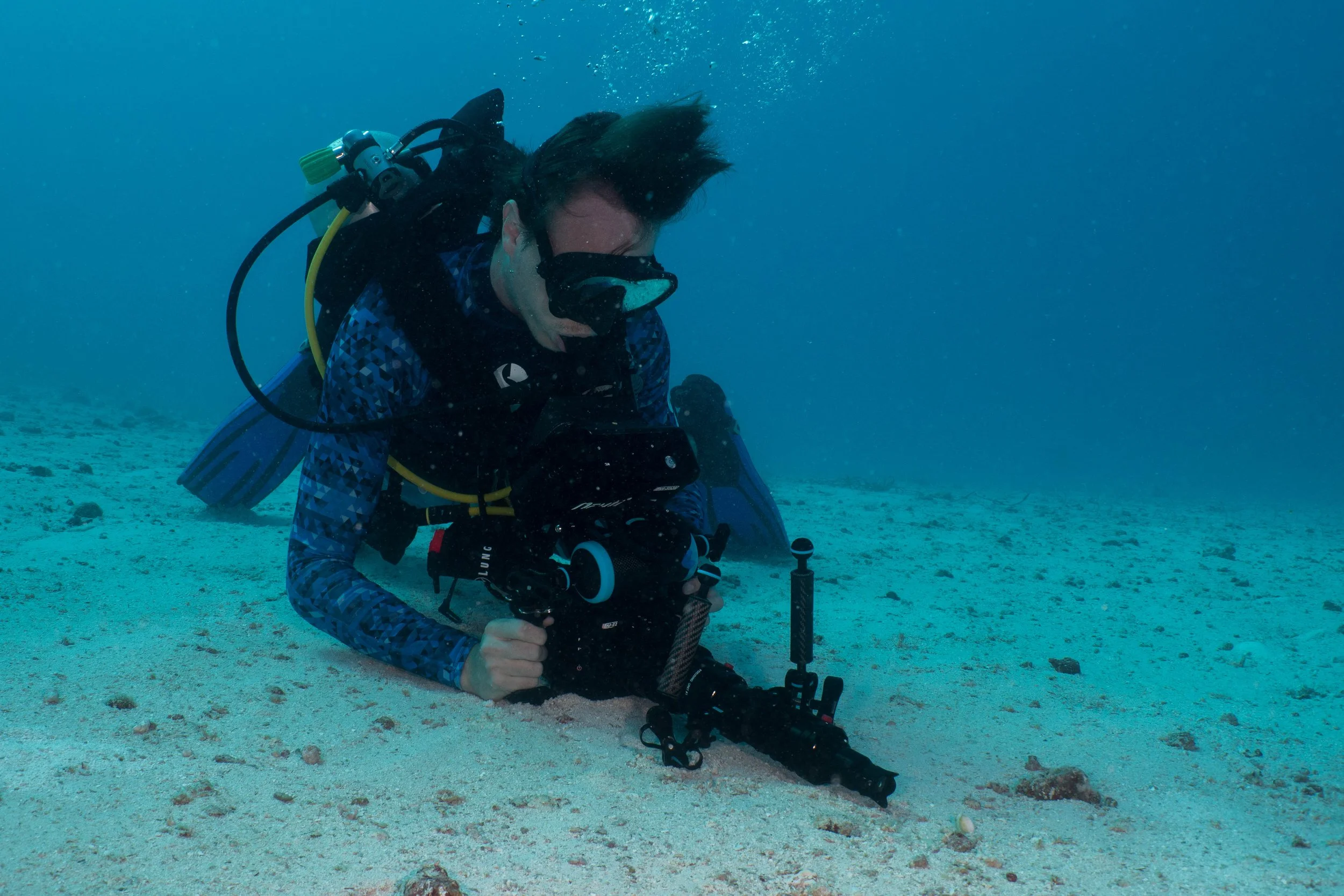 Taucher mit Kamera am Meeresboden, umgeben von Wasser und Sand, beim Tauchen