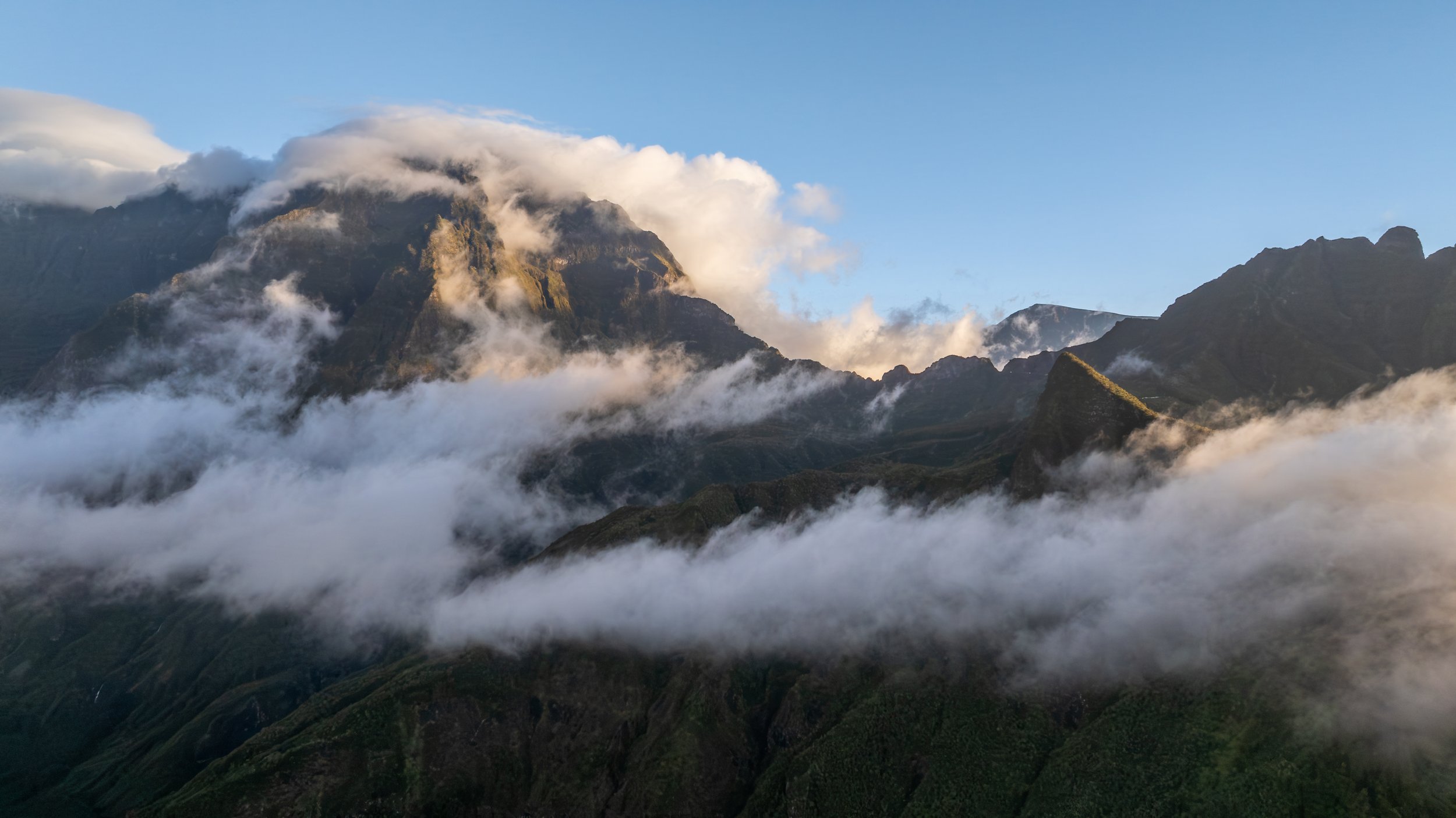 Berglandschaft mit Wolken und Nebel, hohe Berge, teilweise bewaldet, blauer Himmel