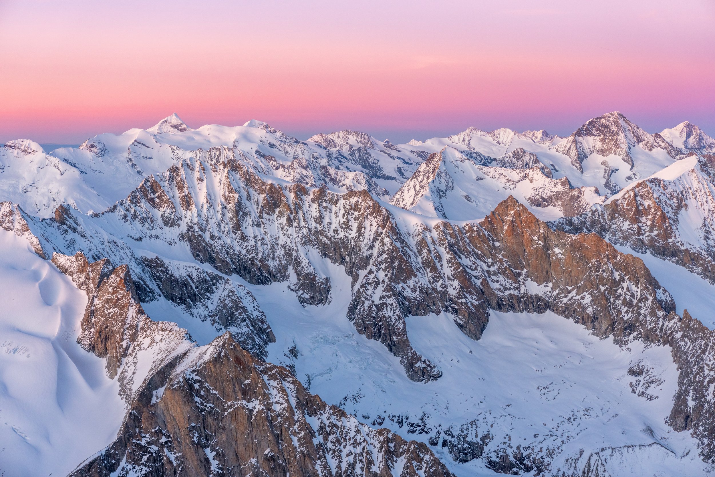 Schneebedeckte Berge bei Sonnenuntergang mit pinkem Himmel.