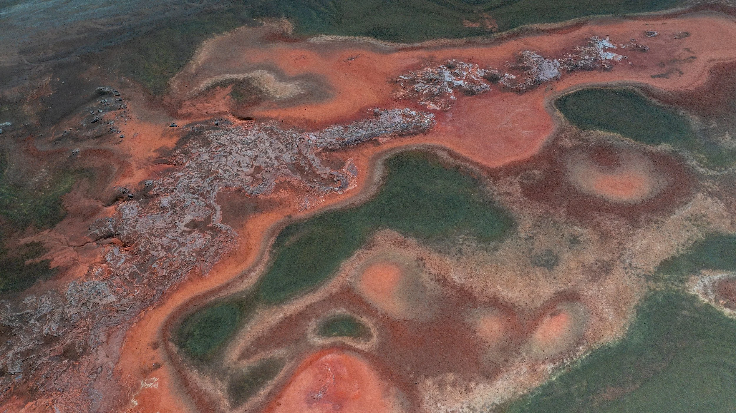 Luftaufnahme einer Seen- und Lava-Landschaft mit roten, grünen und schwarzen Bereichen.