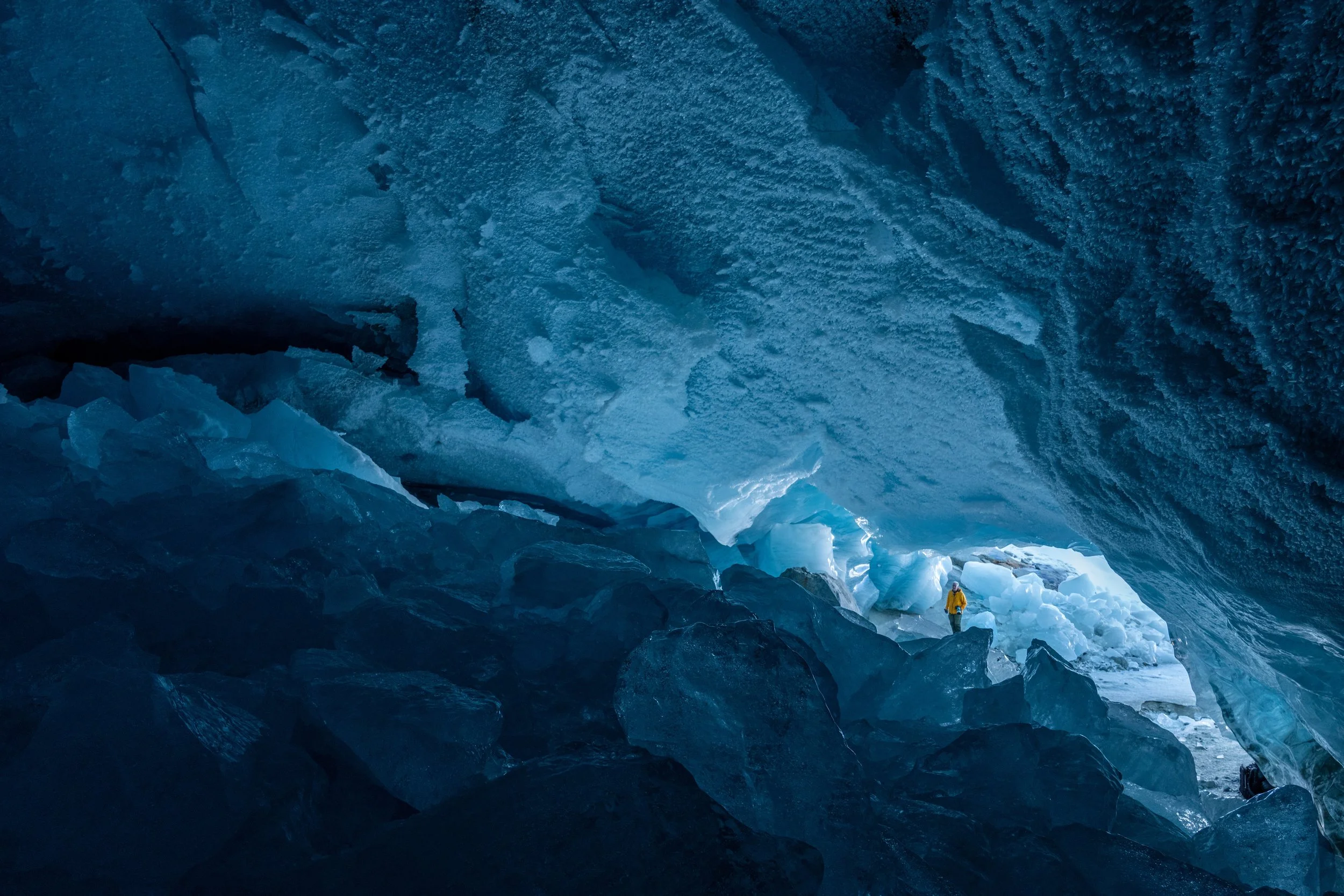 Ein Eiskletterer in einer blauen Eisgrotte mit großen Eiszapfen und Felsen.