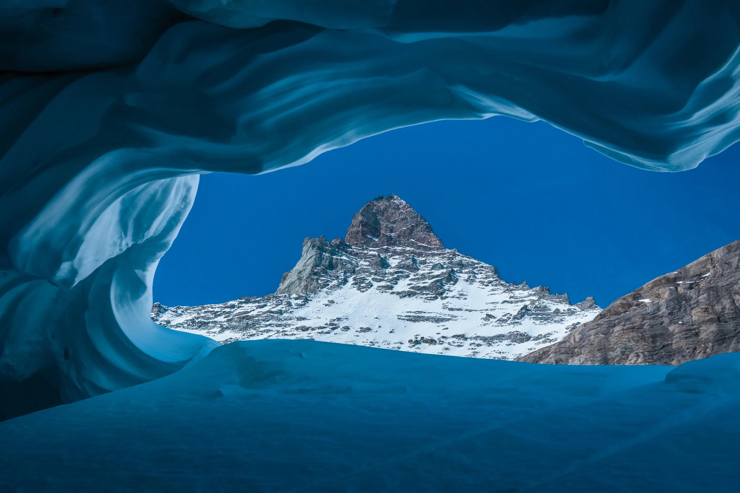Berggipfel mit schnee, sichtbar durch eine Eisgrotte