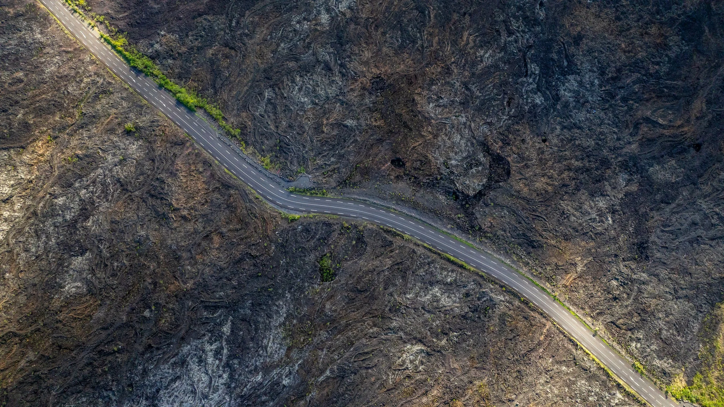 Luftaufnahme einer kurvigen Straße, die durch eine felsige, bergige Landschaft führt.