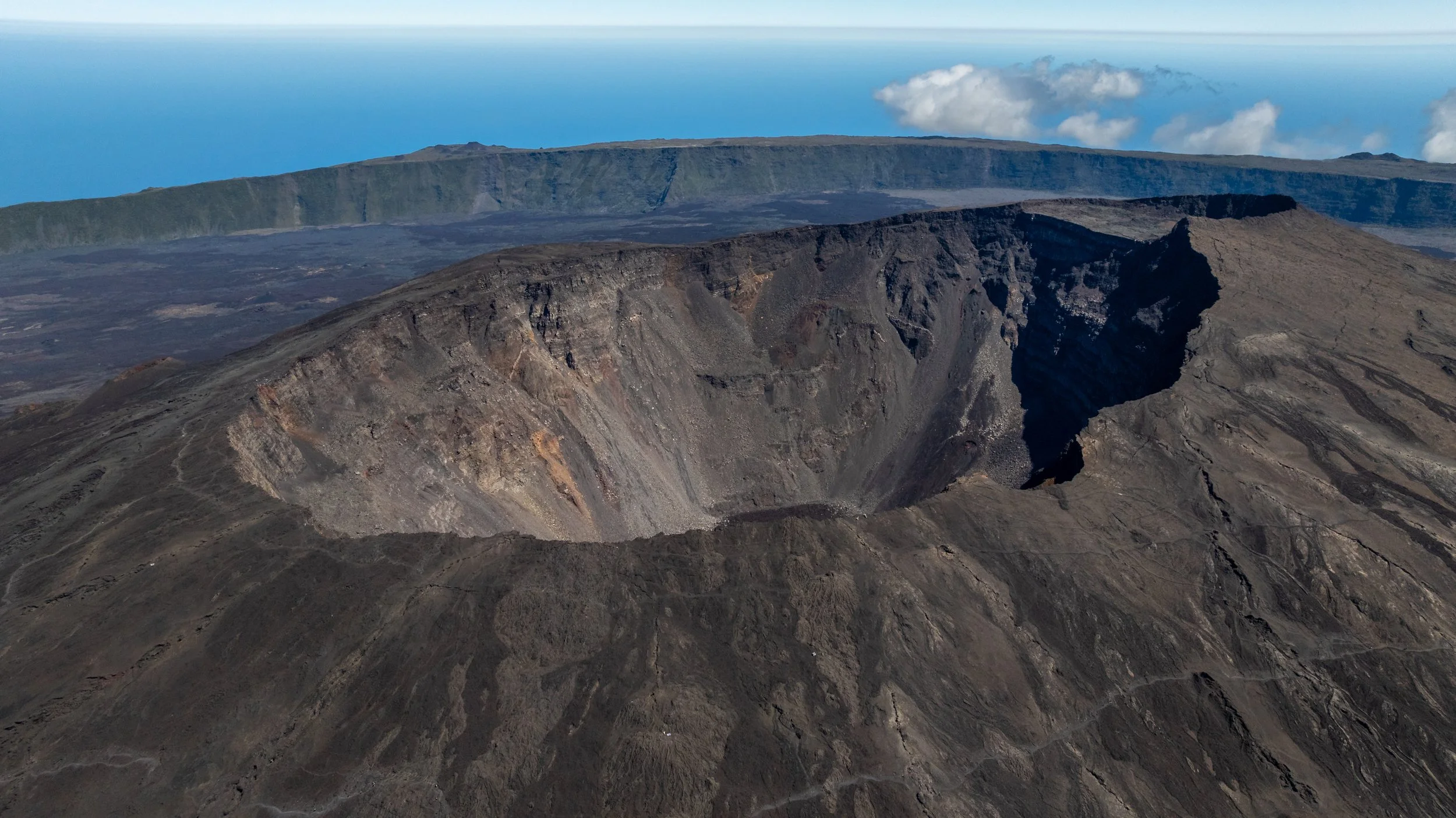 Vulkan mit großer Caldera und dunklem Lavagestein, mit Blick auf den Himmel und das Meer im Hintergrund.