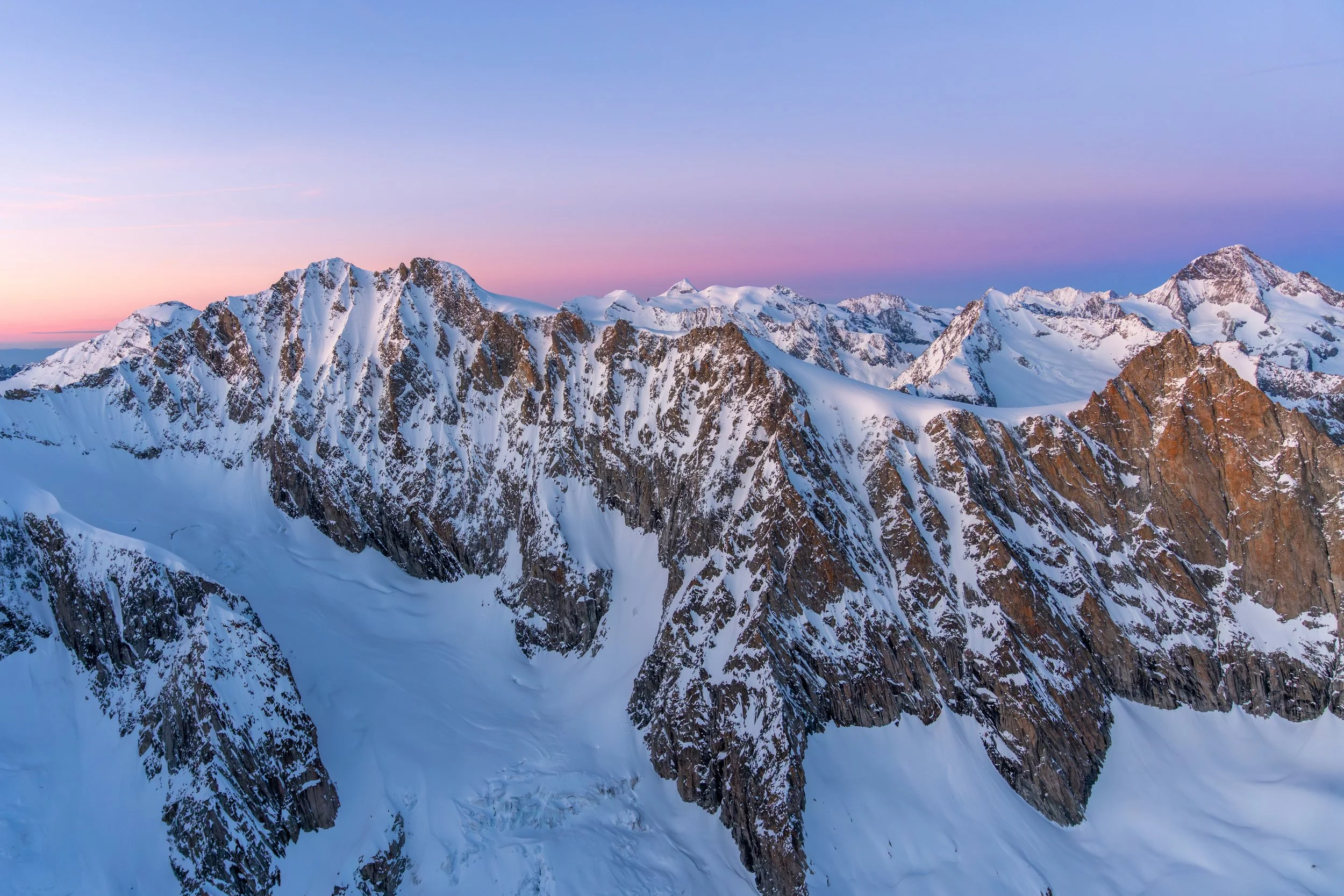 Bergkette mit schneebedeckten Gipfeln bei Sonnenaufgang im Alpengebiet.
