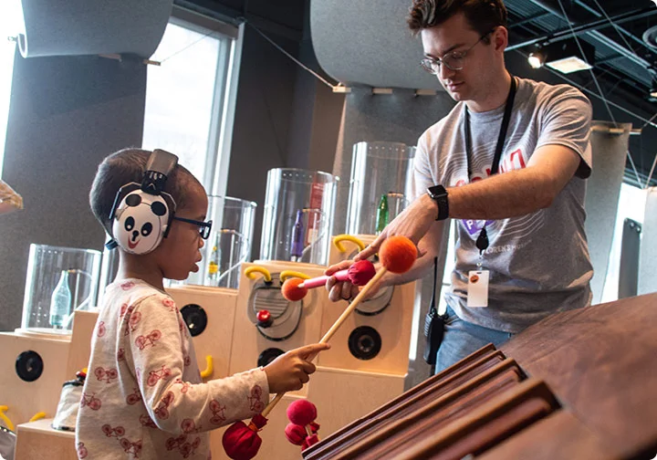 A Chicago Children's Museum staff member teaches a little boy to play a marimba with mallets