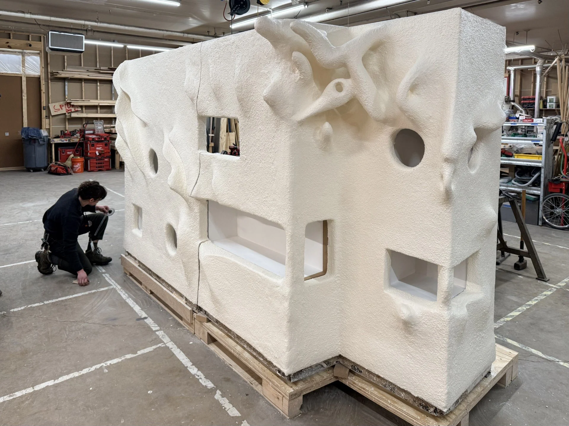 A white sculpture with many holes with a woman bending down to look at it.