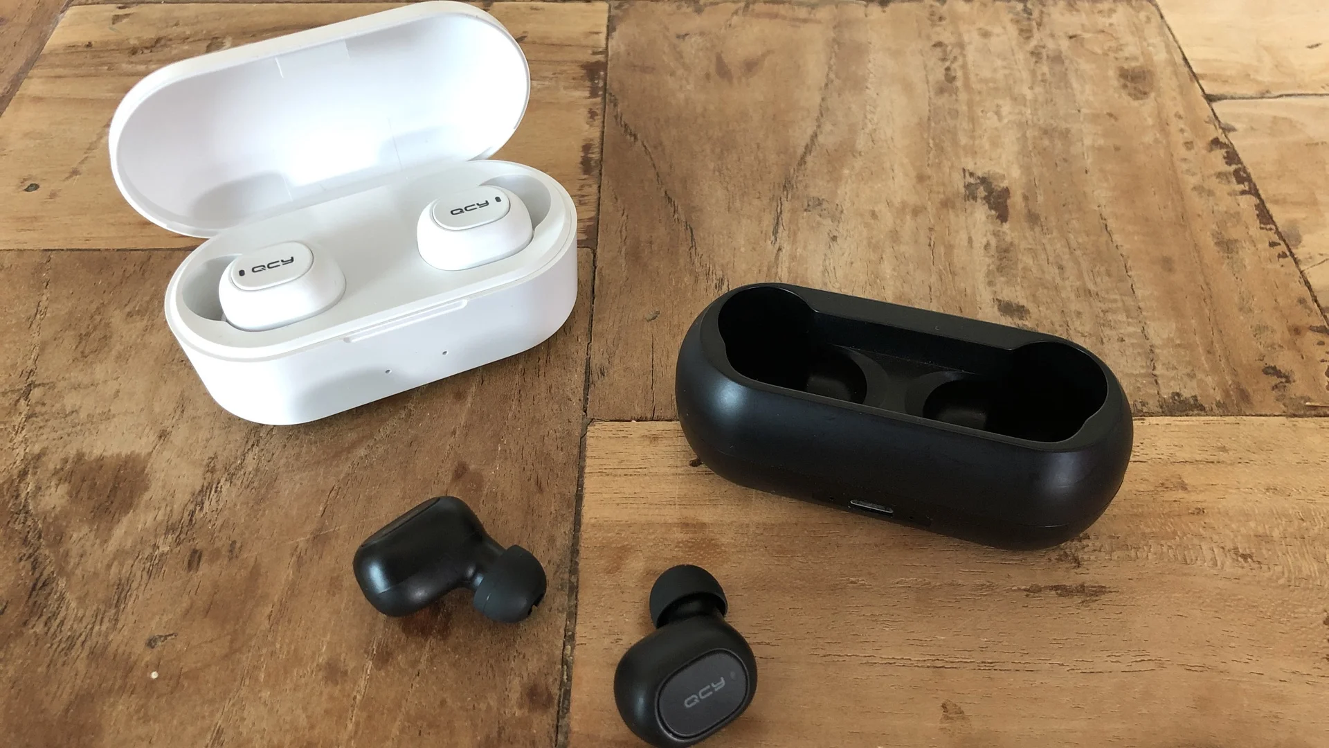 The QCY QS1 in black, versus the QCY QS2 in white - which are the same earphones, just with a bigger charging case