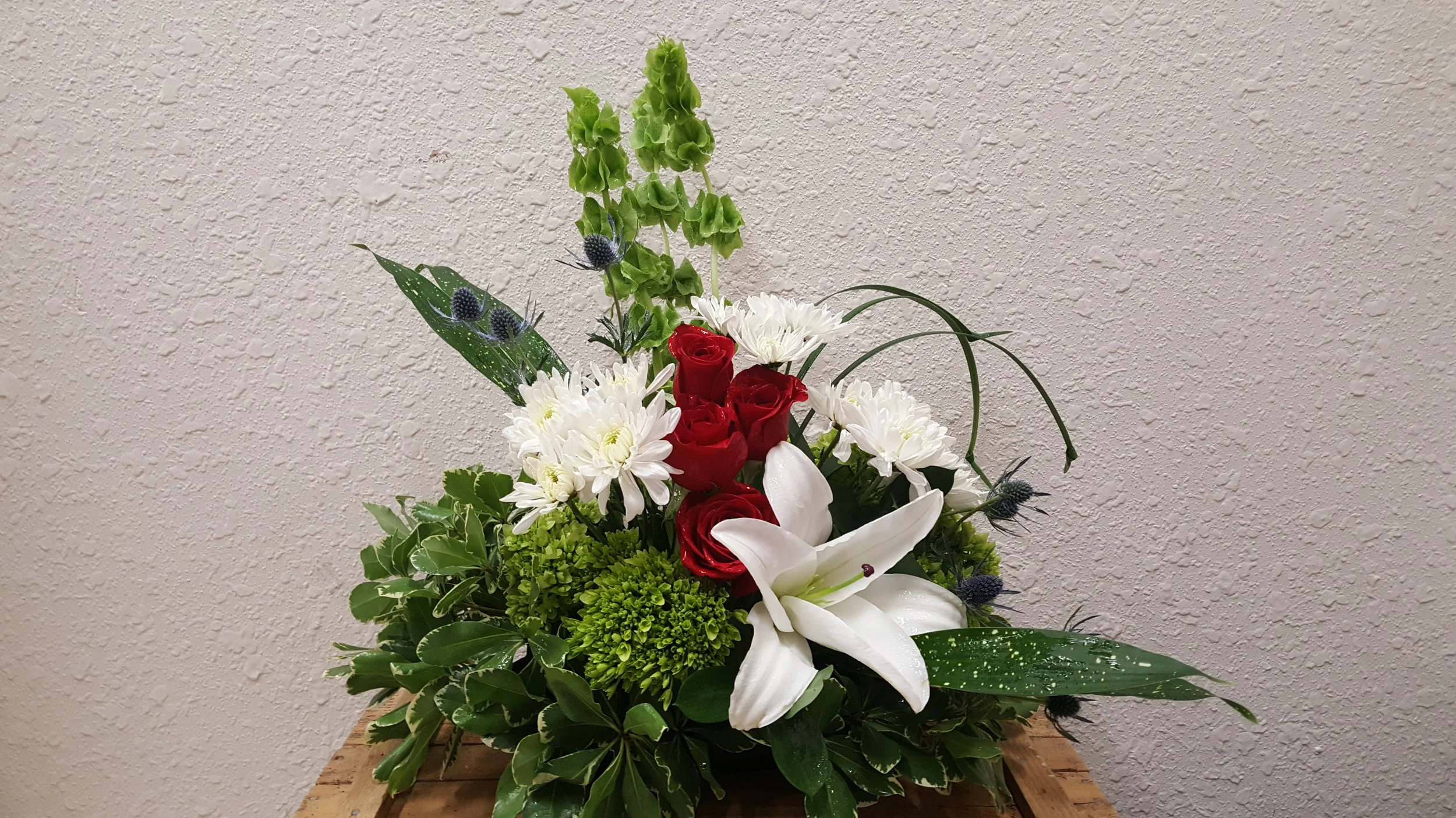 White lilies, hydrangeas, crimson peonies, white spider mums and stately bells of ireland fill out this polished memorial piece.