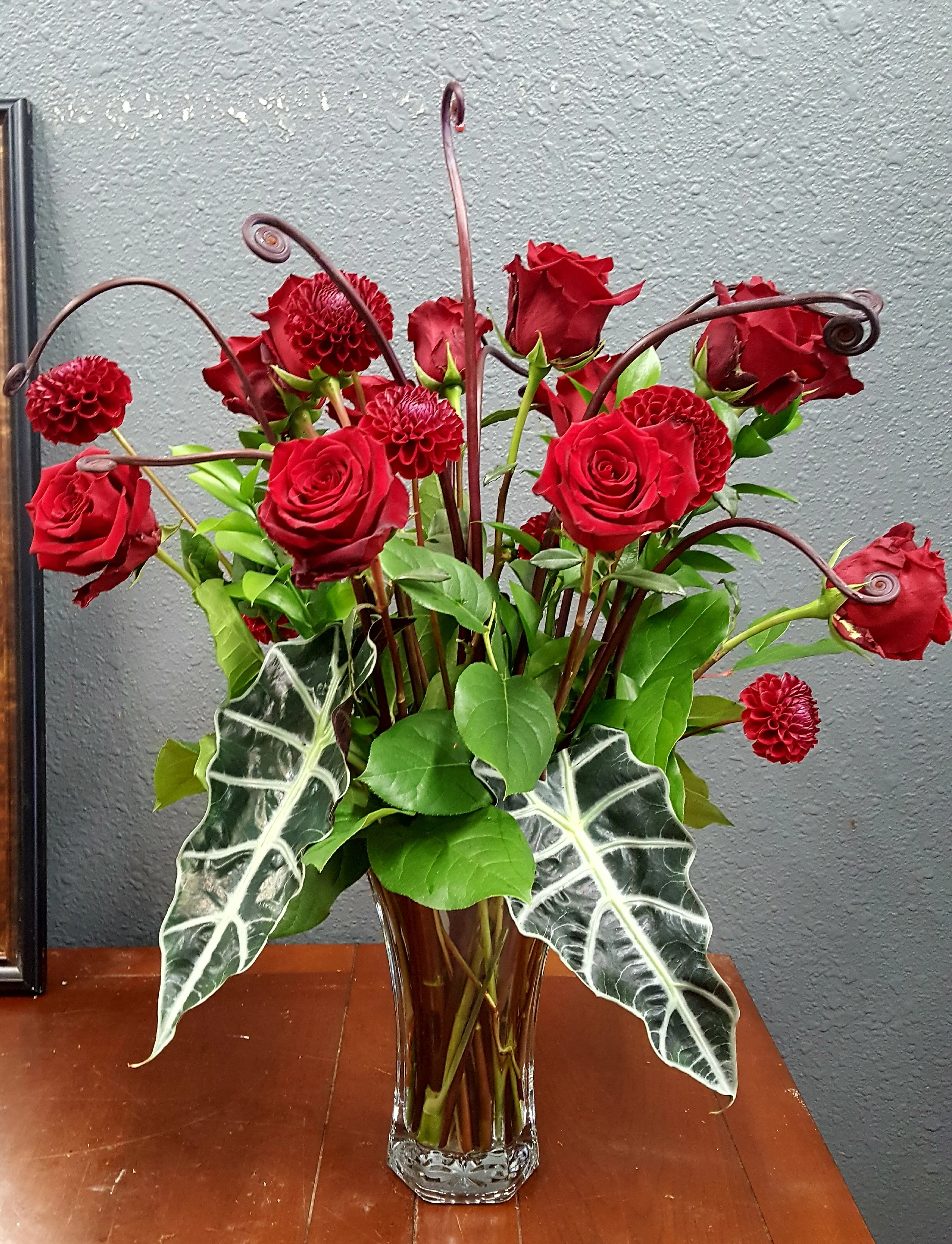A dozen red roses in a one of a kind, custom order. Tropical leaves and fern shoots take a classic arrangement to an entirely new level.