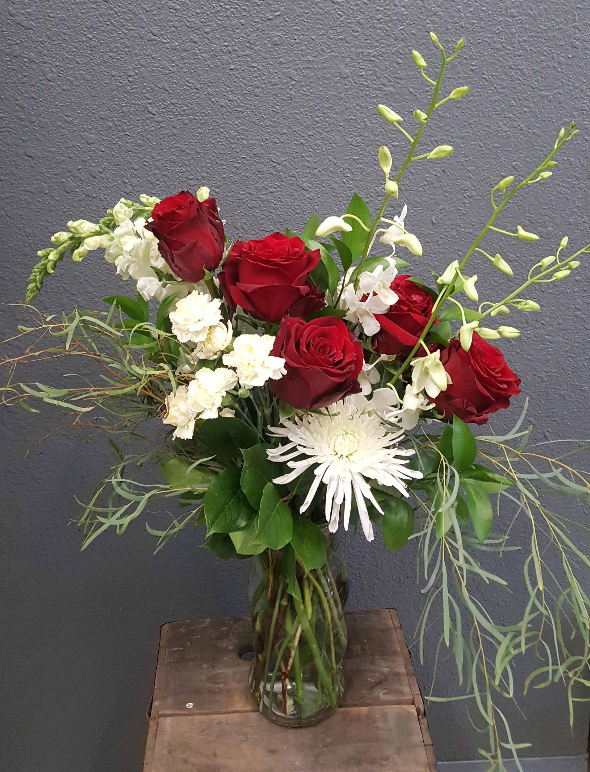 Vivid red roses, white snapdragons, orchids and chrysanthemums are softened by the draping eucalyptus.