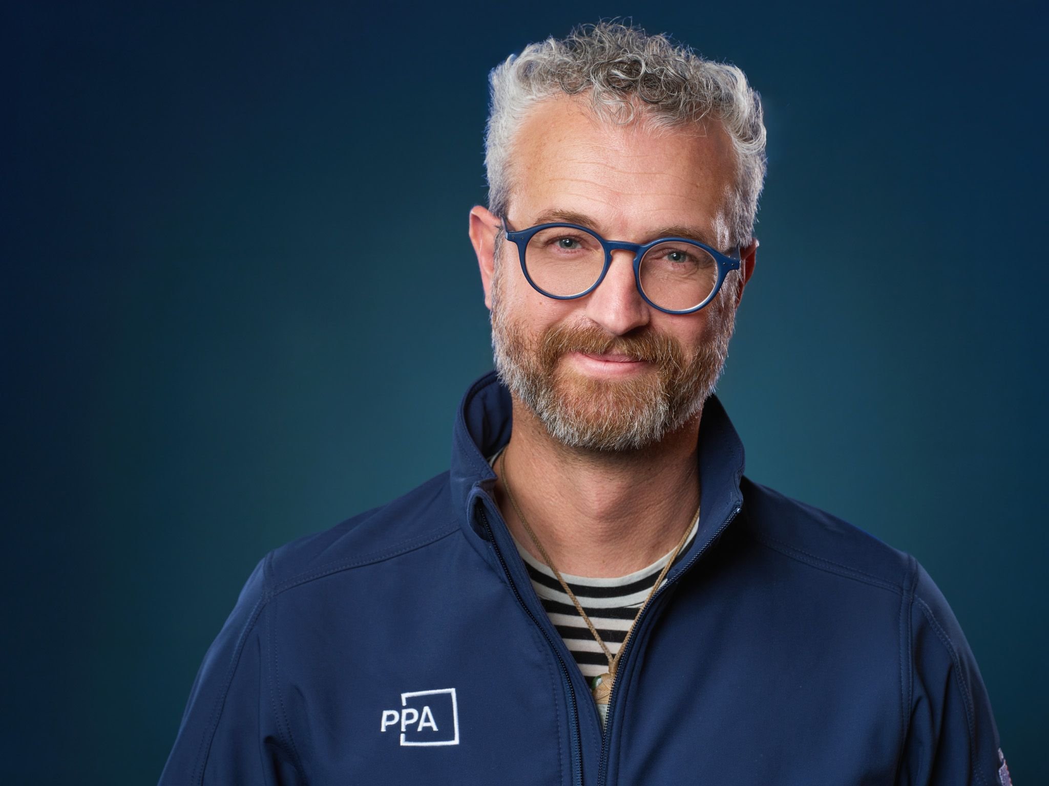 Jeffrey Packard portrait on blue-green background with World Photographic Cup Team USA blue jacket.